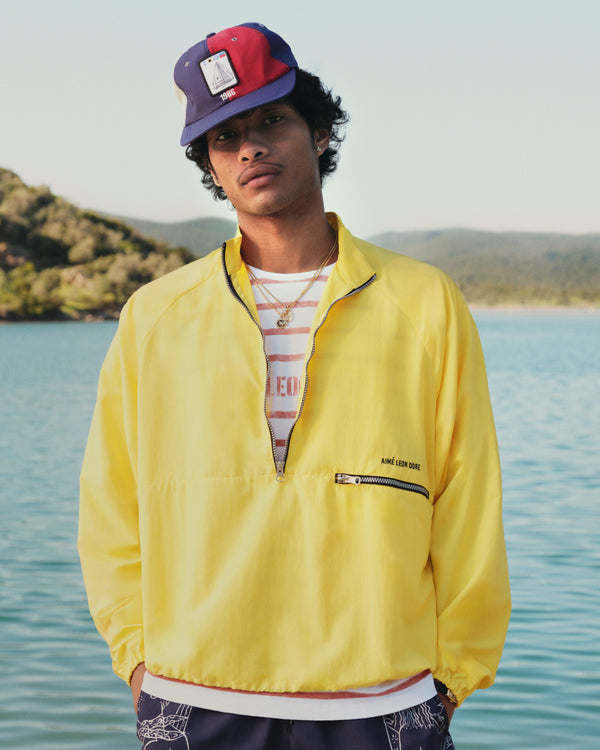 A person in a Slub Beach Tee stands by a lake with hills and trees in the background.