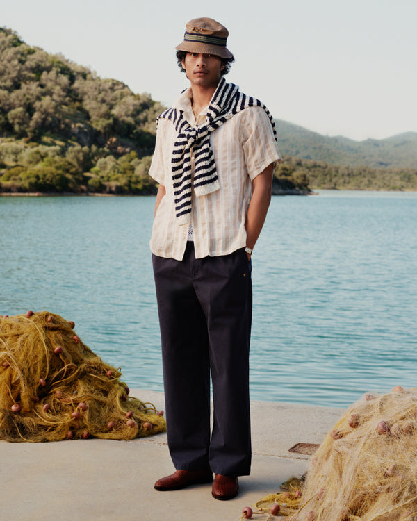 A man stands by a lake wearing the Linen Blend Striped Camp Shirt draped over his shoulders.