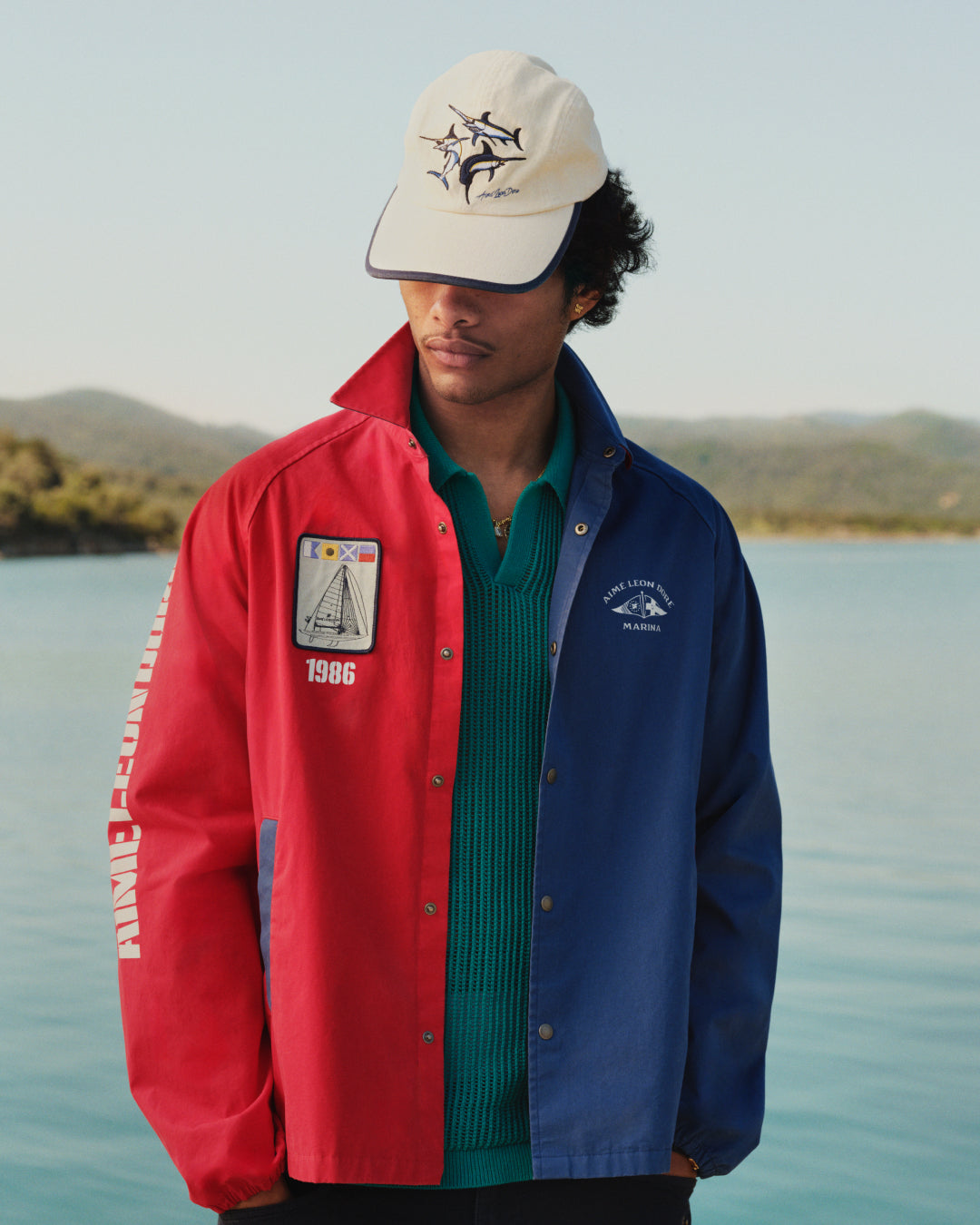 Wearing the Marina Jacket, a person stands outdoors near water with hills in the background.