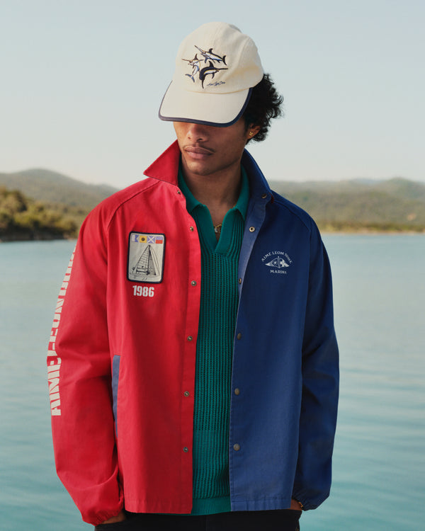 Wearing the Marina Jacket, a person stands outdoors near water with hills in the background.