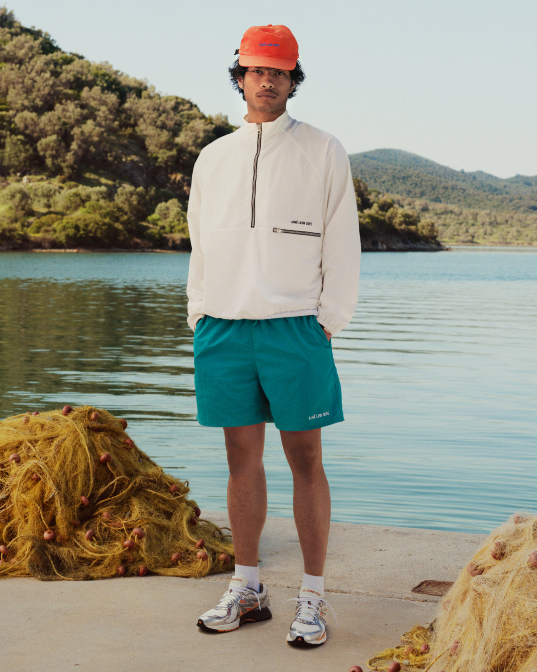 A person in ALD / New Balance 860v2 shoes stands by a lake with fishing nets and hills in the background.
