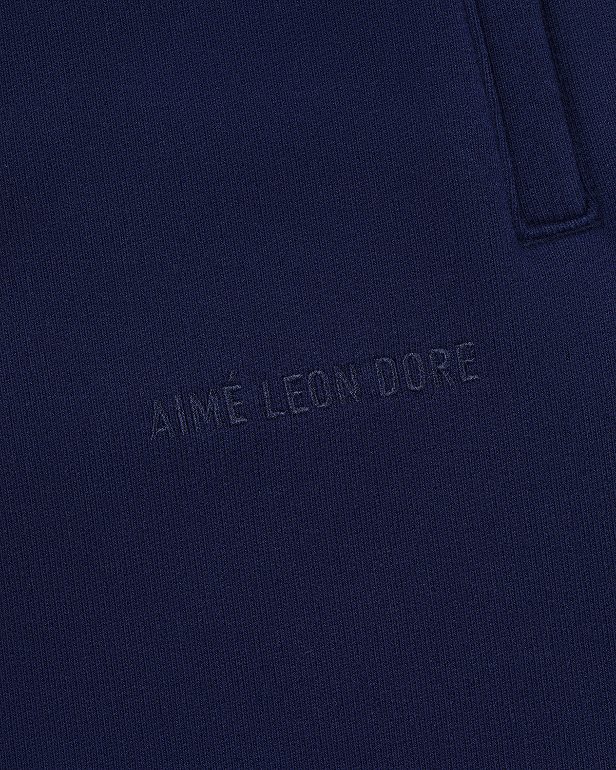Close-up of navy blue Tonal Logo Sweatpants with AIMÉ LEON DORE subtly embossed near the pocket seam.