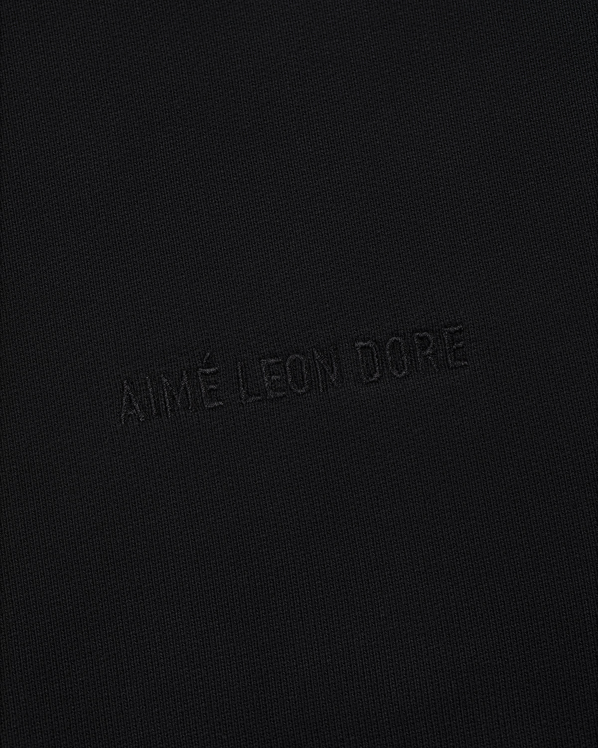The Tonal Logo Hoodie features black textured fabric with AIMÉ LEON DORE subtly embossed in matching black thread.
