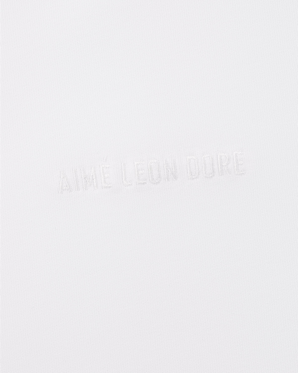 Long-Sleeve Tonal Logo Tee features white fabric with AIMÉ LEON DORE subtly embossed, blending into the background.