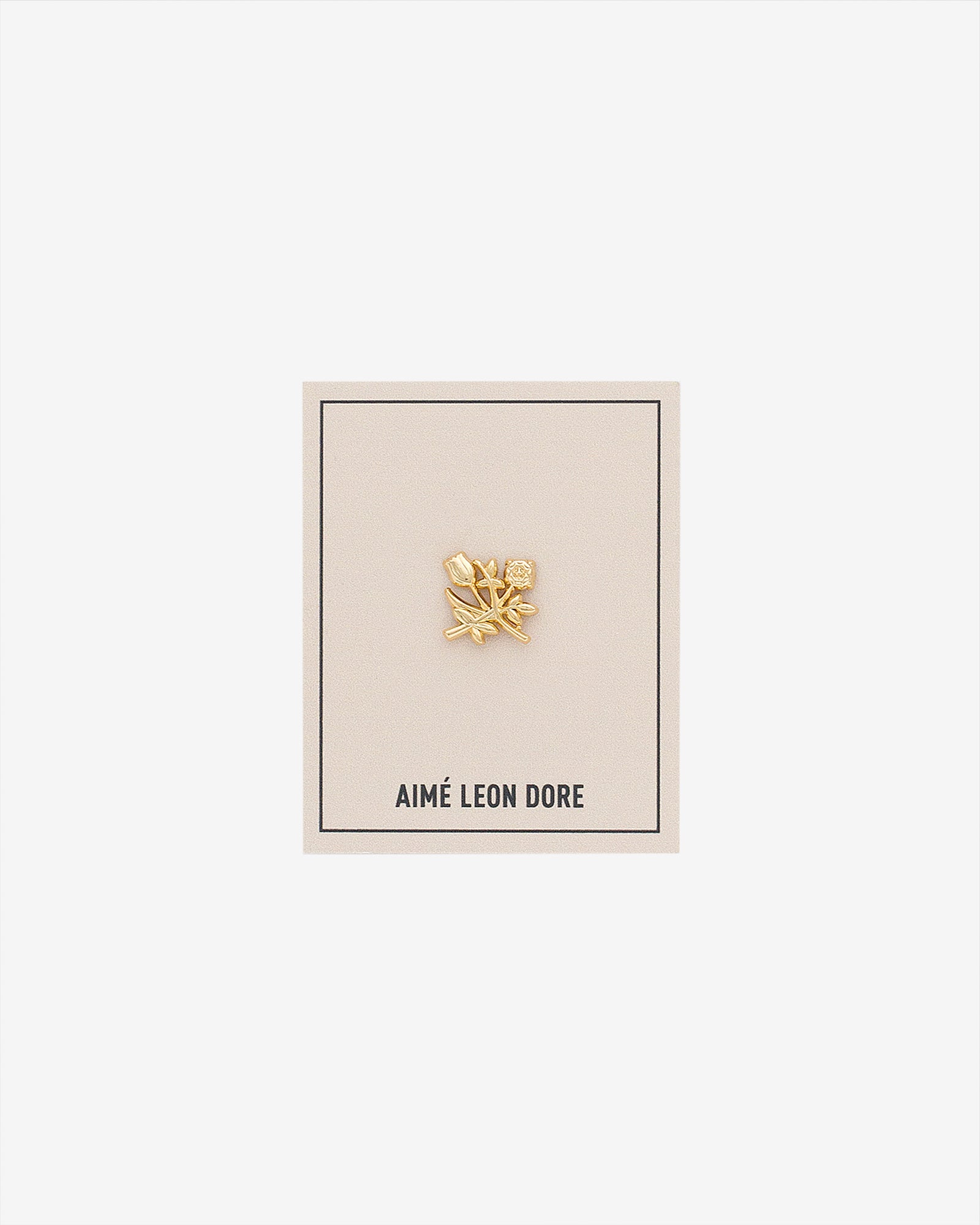 ALD Pin: Gold floral design with small gem, on cream AIMÉ LEON DORE card with thin black border.