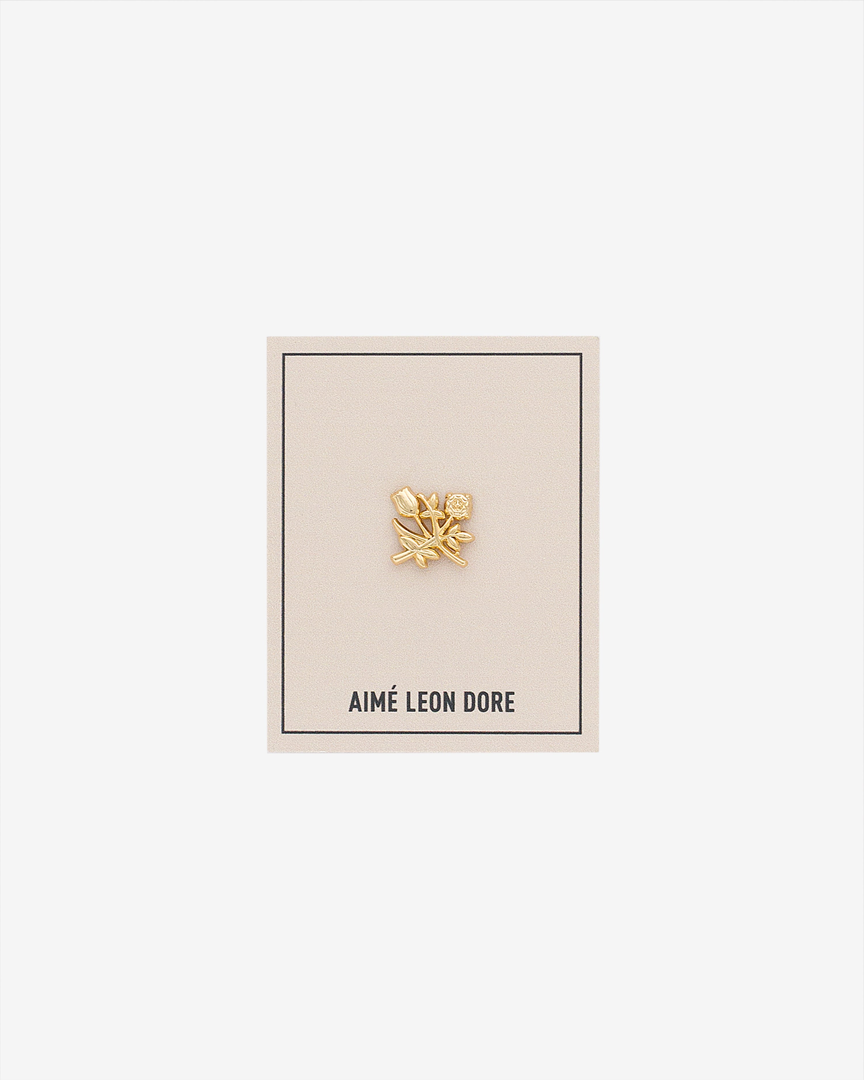 ALD Pin: Gold floral design with small gem, on cream AIMÉ LEON DORE card with thin black border.