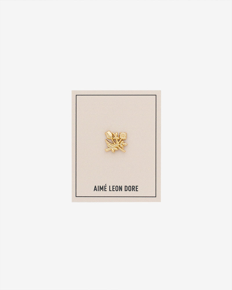 ALD Pin: Gold floral design with small gem, on cream AIMÉ LEON DORE card with thin black border.