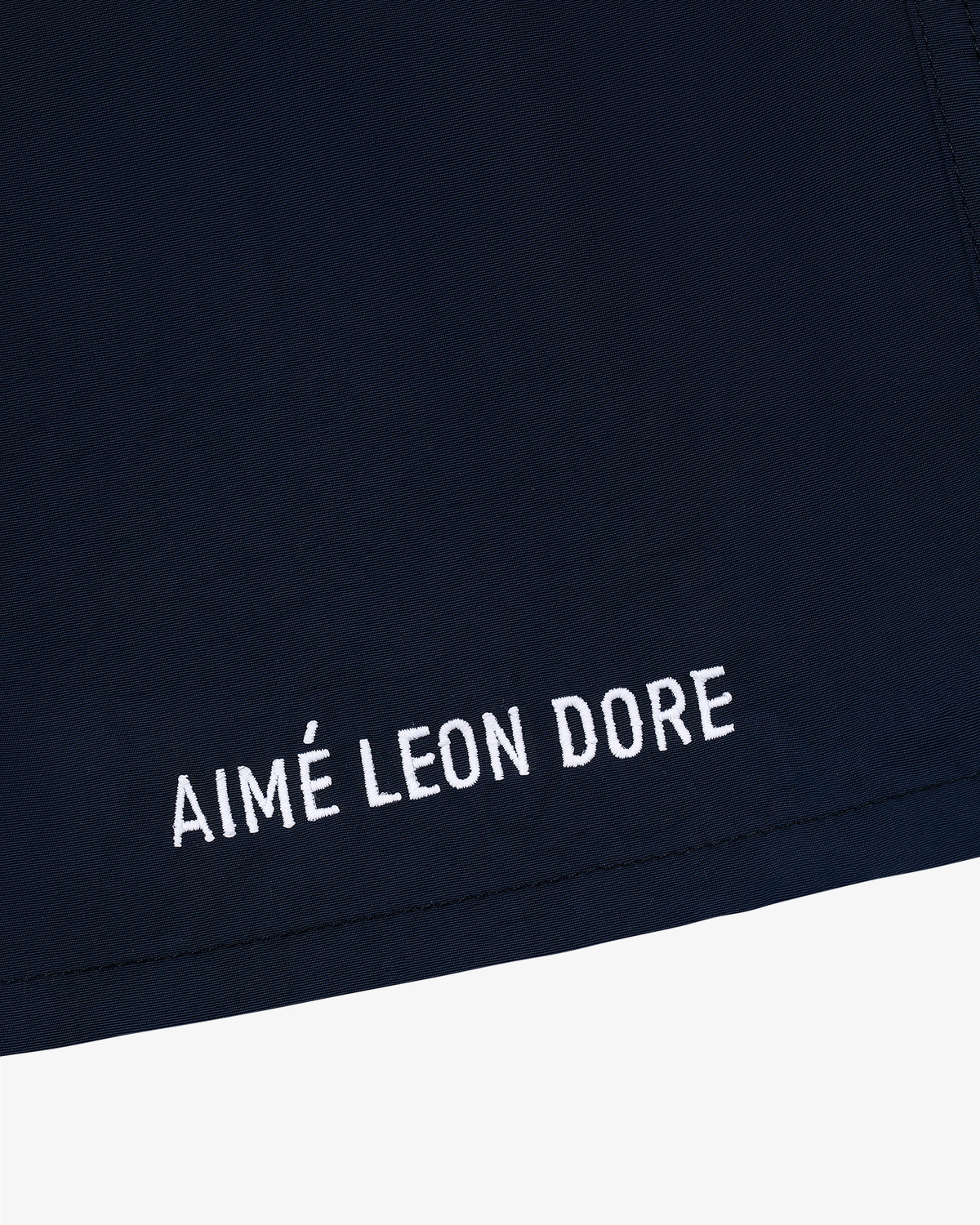Close-up of navy blue Core Nylon Short with AIMÉ LEON DORE embroidered in white near the edge.