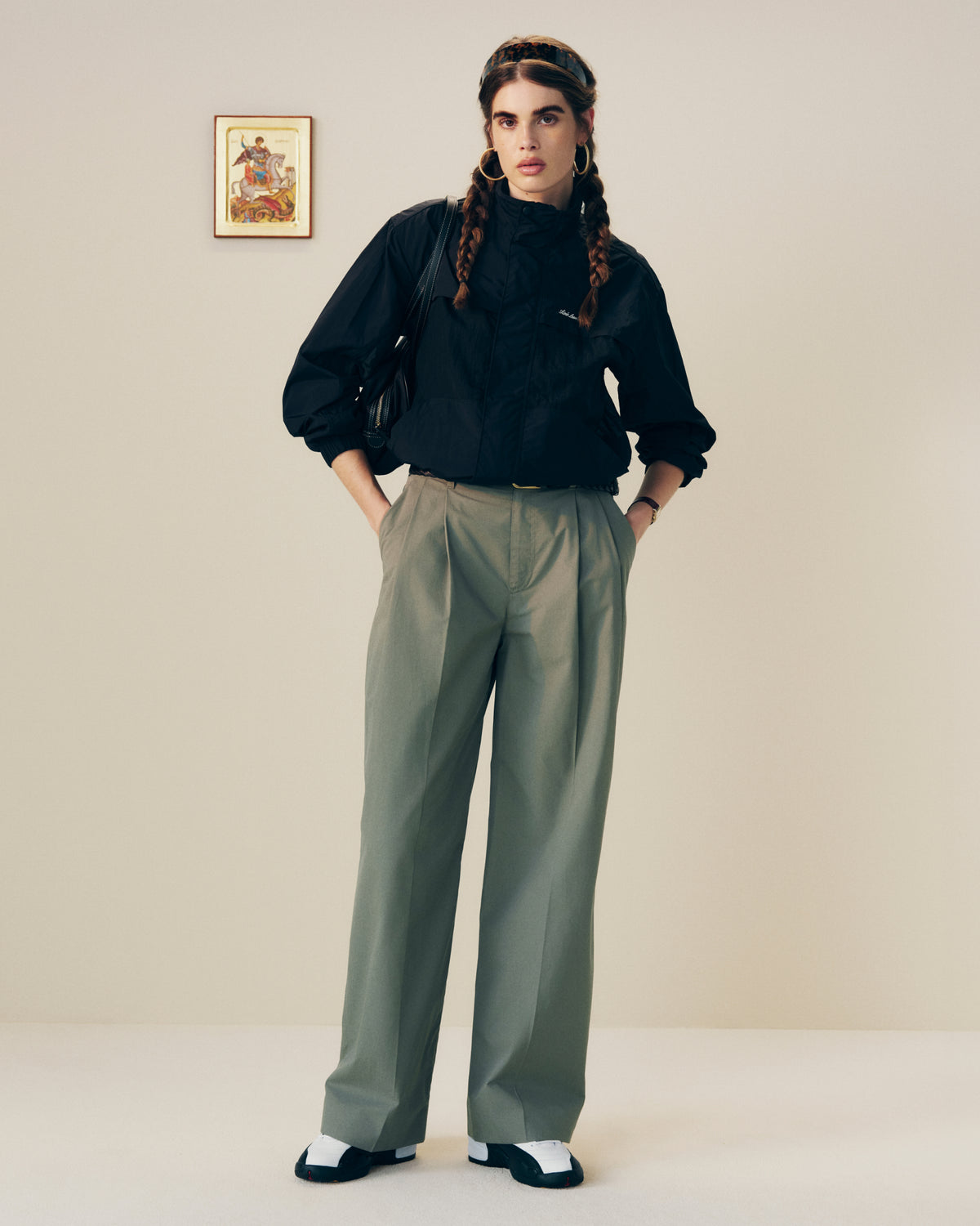 Person with long braided hair wears a black top and Lightweighted Pleated Cotton Trouser in a minimal room.