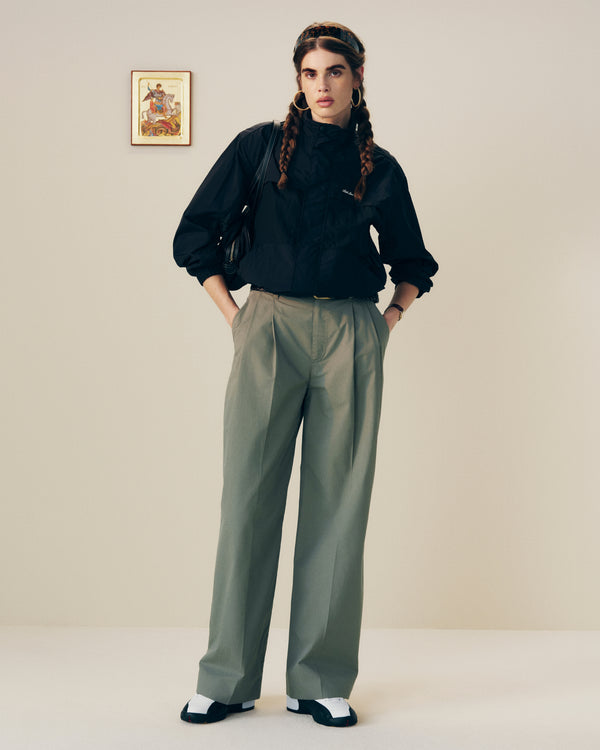 Person with long braided hair wears a black top and Lightweighted Pleated Cotton Trouser in a minimal room.