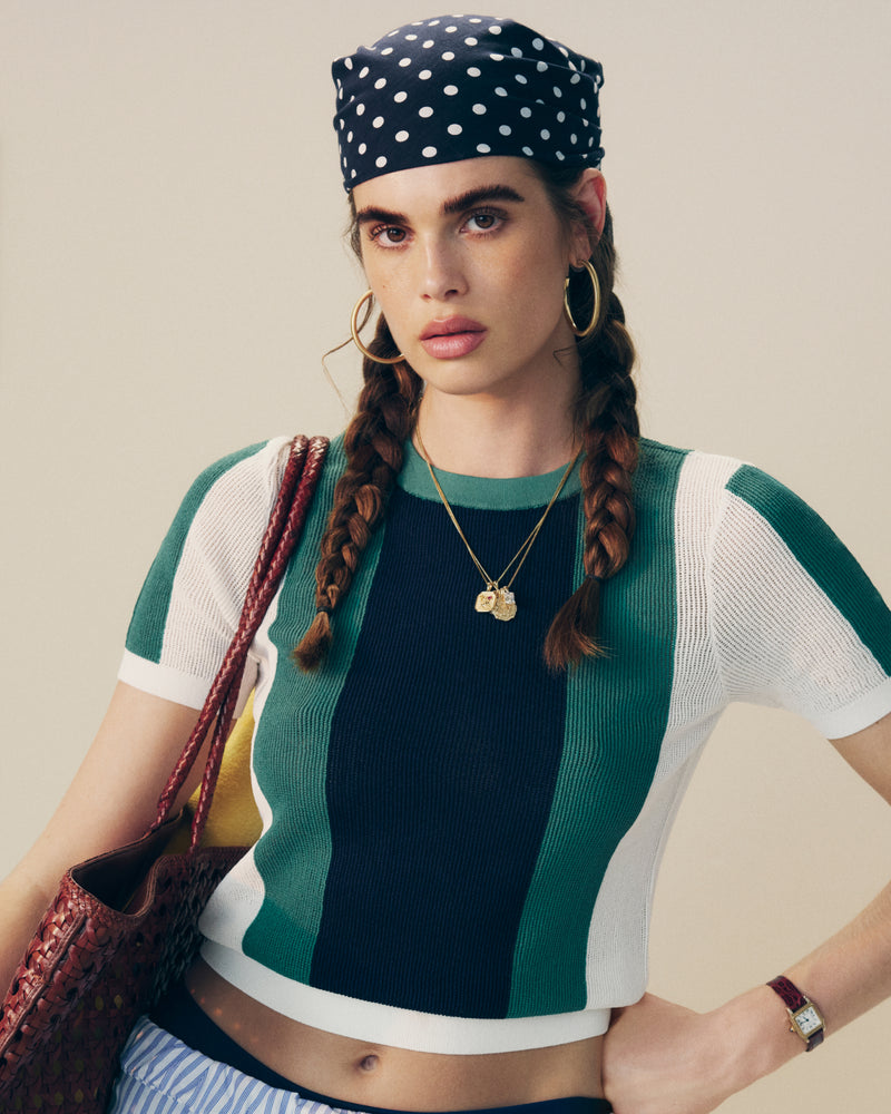 Woman with long braids wears a polka dot headscarf, hoop earrings, Striped Mesh Knit Tee, and carries a red bag.