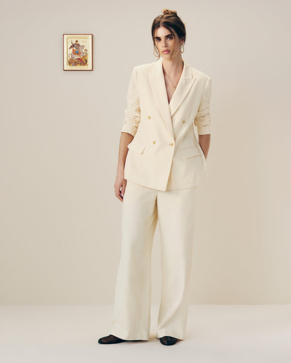 Woman wears Drawstring Cotton Blend Suit Trouser and stands indoors near a small framed picture on a plain wall.