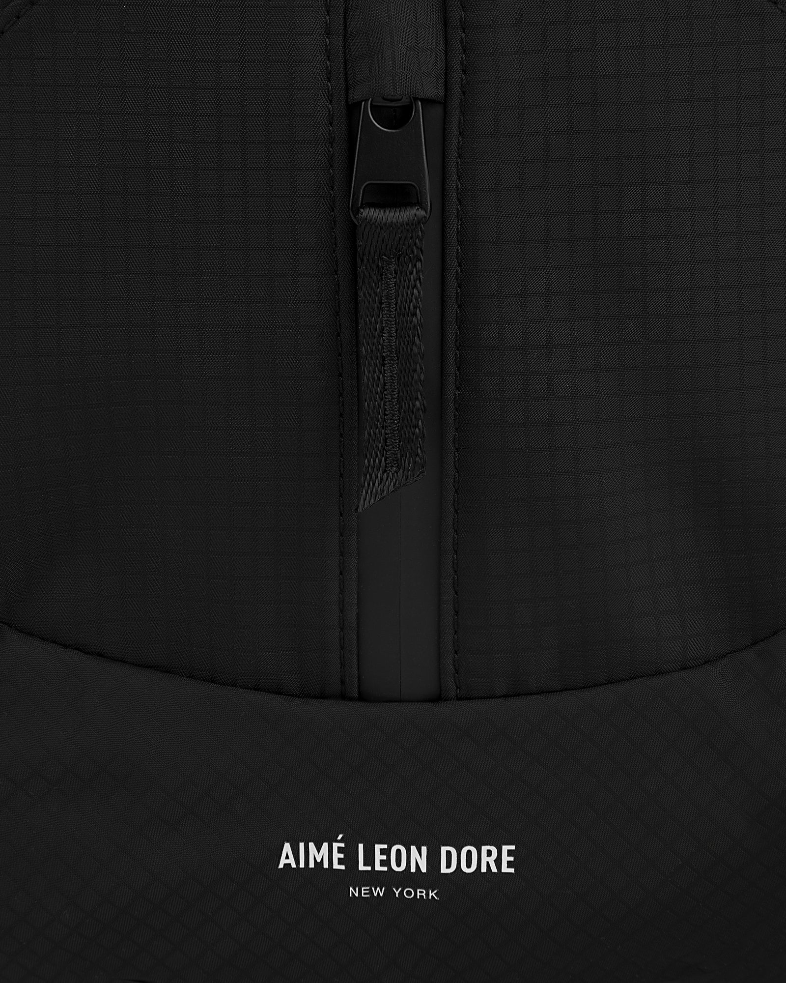 Close-up of a black textured Nylon Messenger Bag with a zipper and AIMÉ LEON DORE NEW YORK printed in white at the bottom.