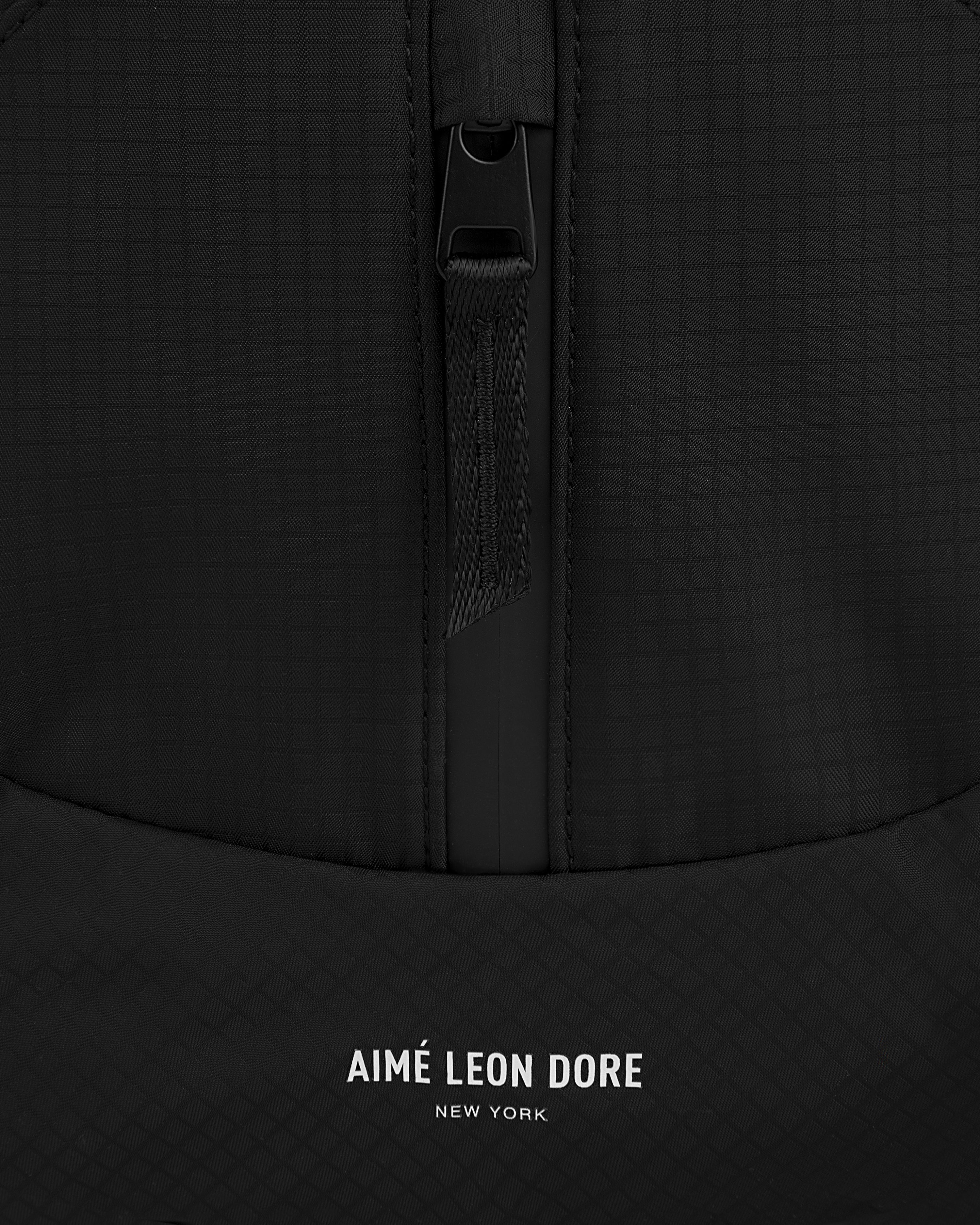 Close-up of a black textured Nylon Messenger Bag with a zipper and AIMÉ LEON DORE NEW YORK printed in white at the bottom.