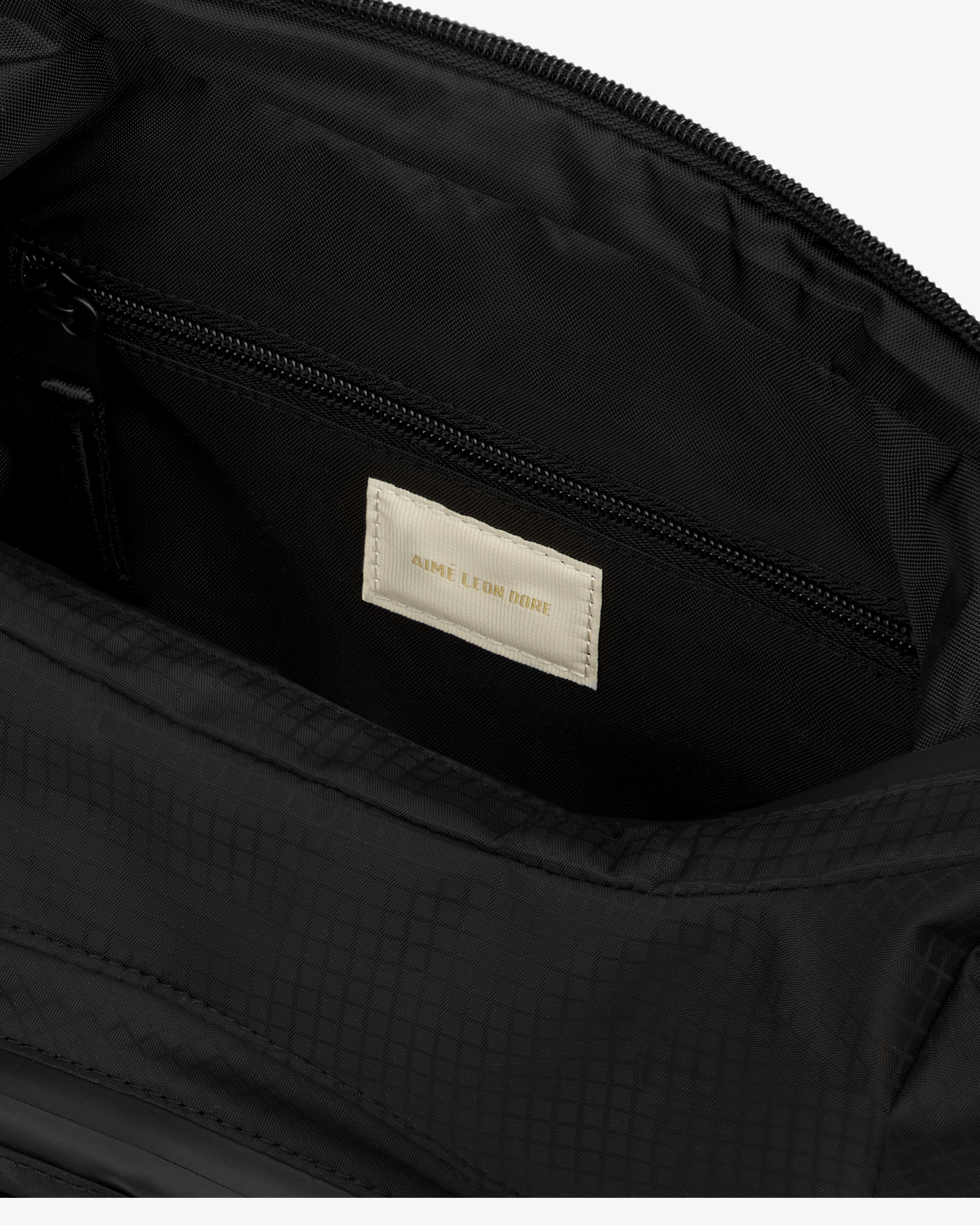 Close-up of a black Nylon Messenger Bag with a beige "AIME LEON DORE" label inside.