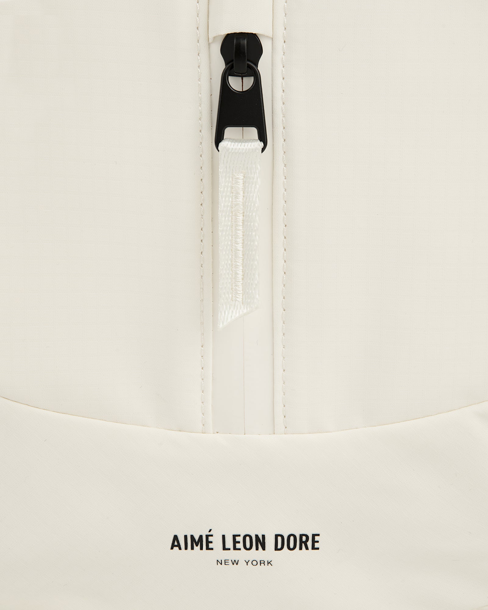 Close-up of a white Nylon Messenger Bag with a zipper and Aimé Leon Dore New York printed near the bottom.