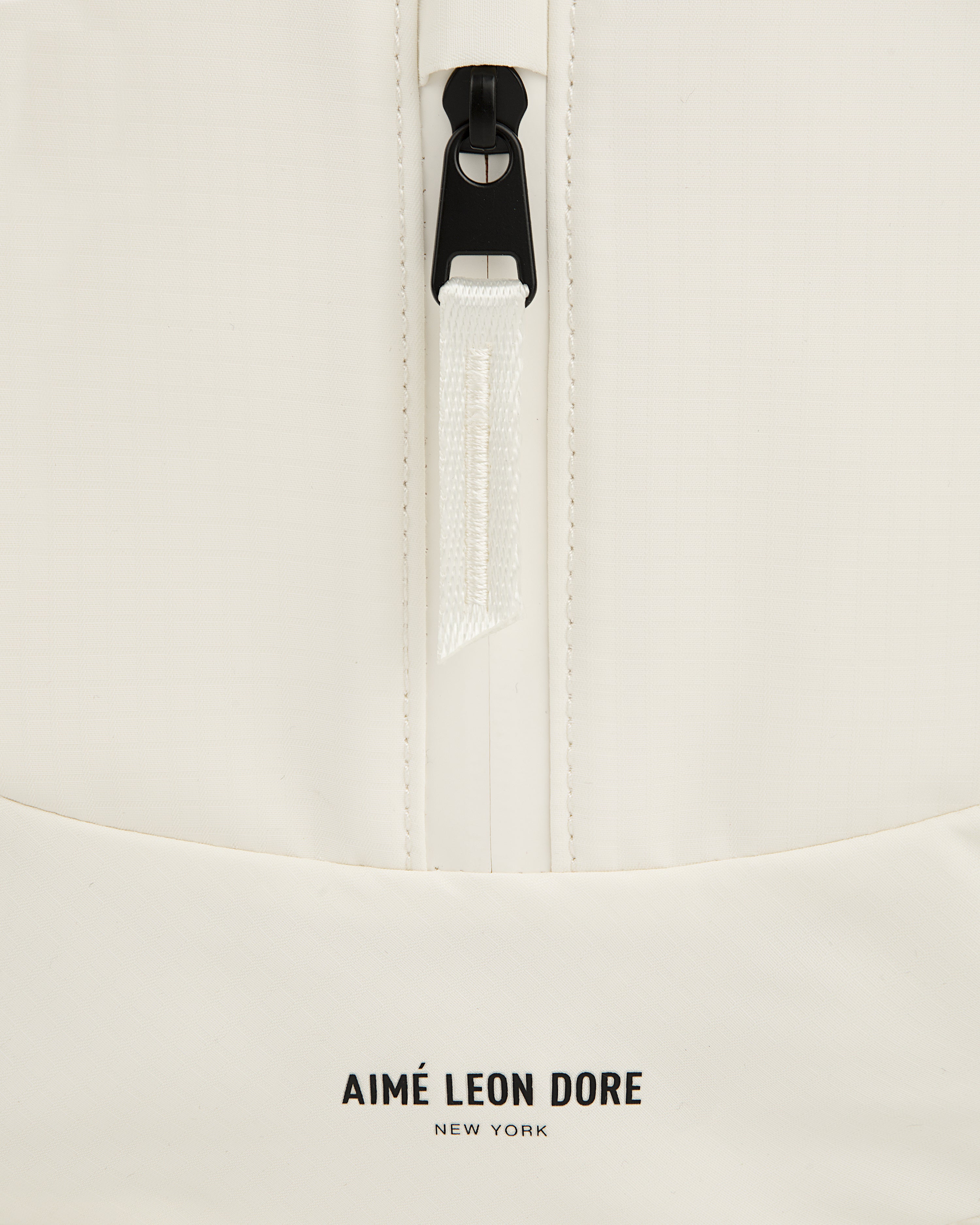 Close-up of a white Nylon Messenger Bag with a zipper and Aimé Leon Dore New York printed near the bottom.
