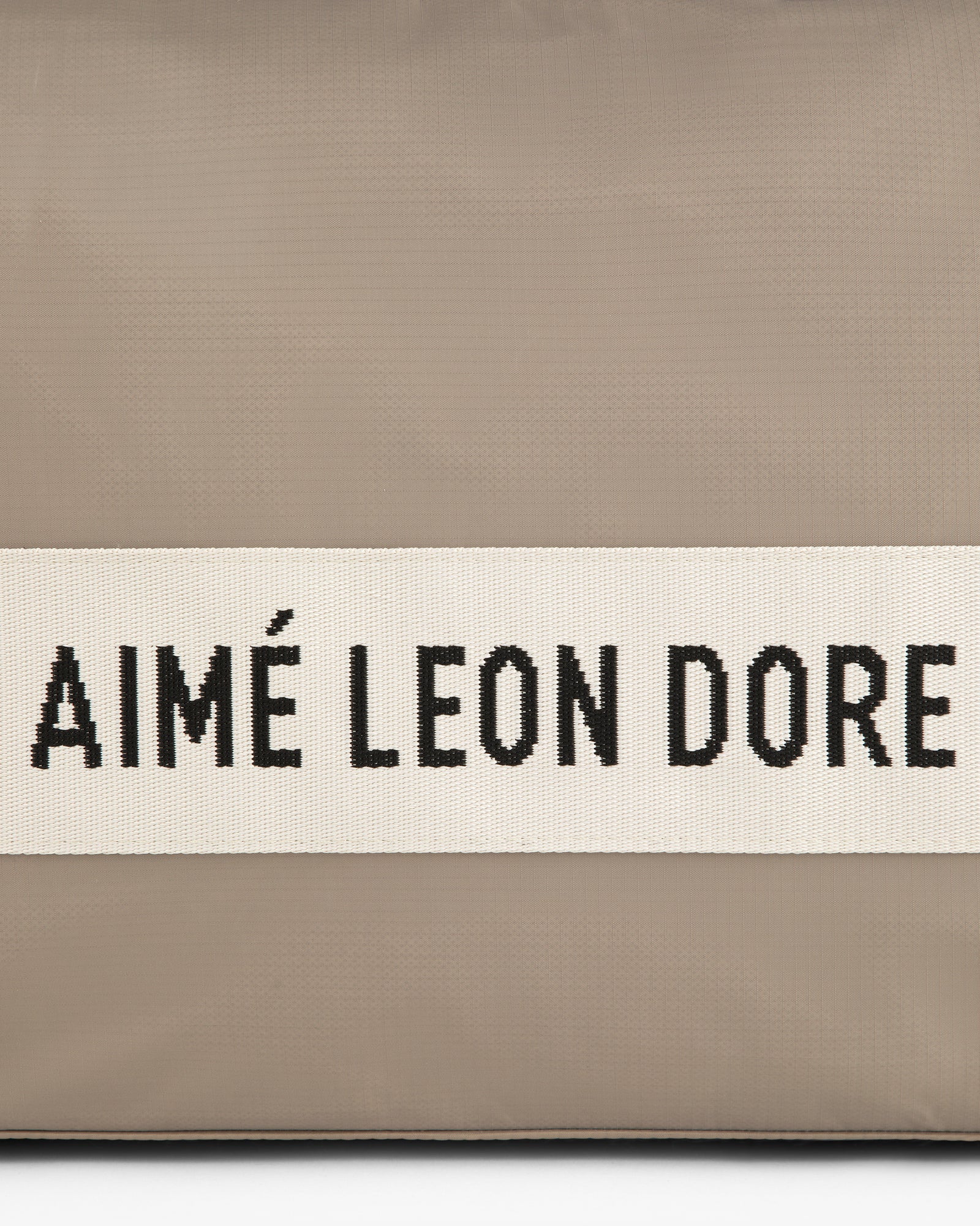 A beige Nylon Duffle Bag with a white band and black AIMÉ LEON DORE text across the center.