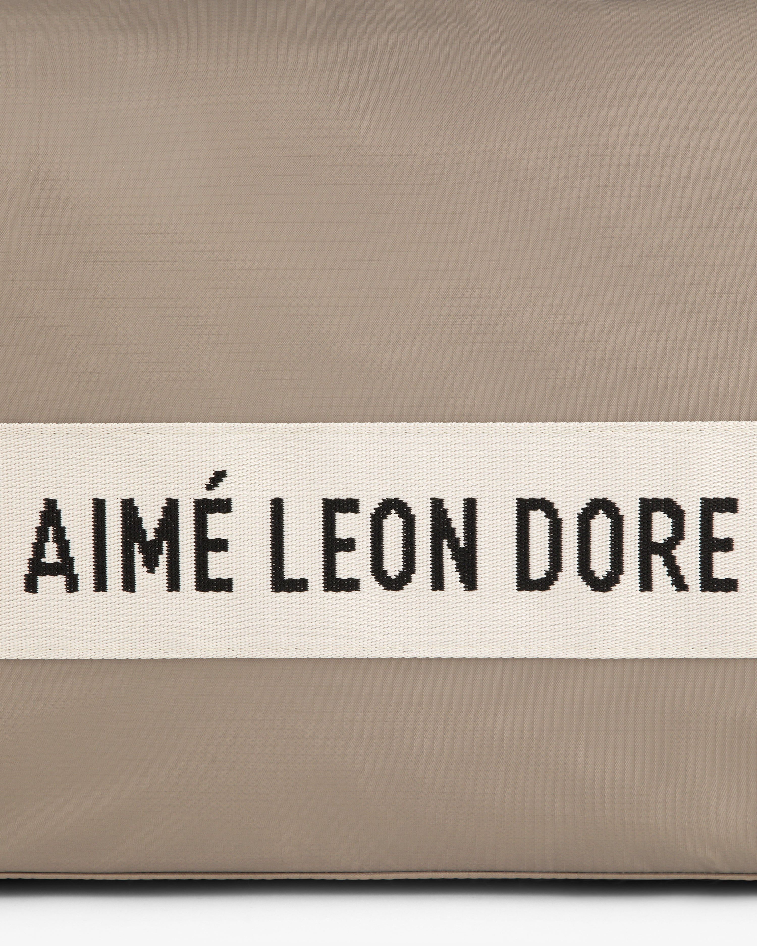 A beige Nylon Duffle Bag with a white band and black AIMÉ LEON DORE text across the center.
