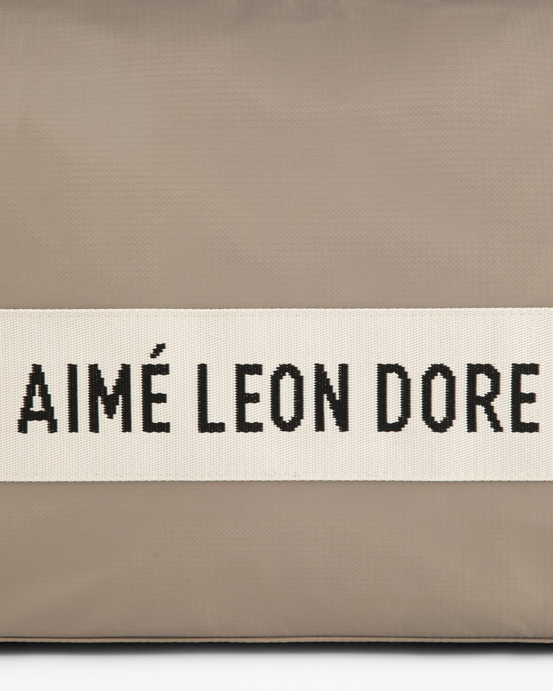 A beige Nylon Duffle Bag with a white band and black AIMÉ LEON DORE text across the center.
