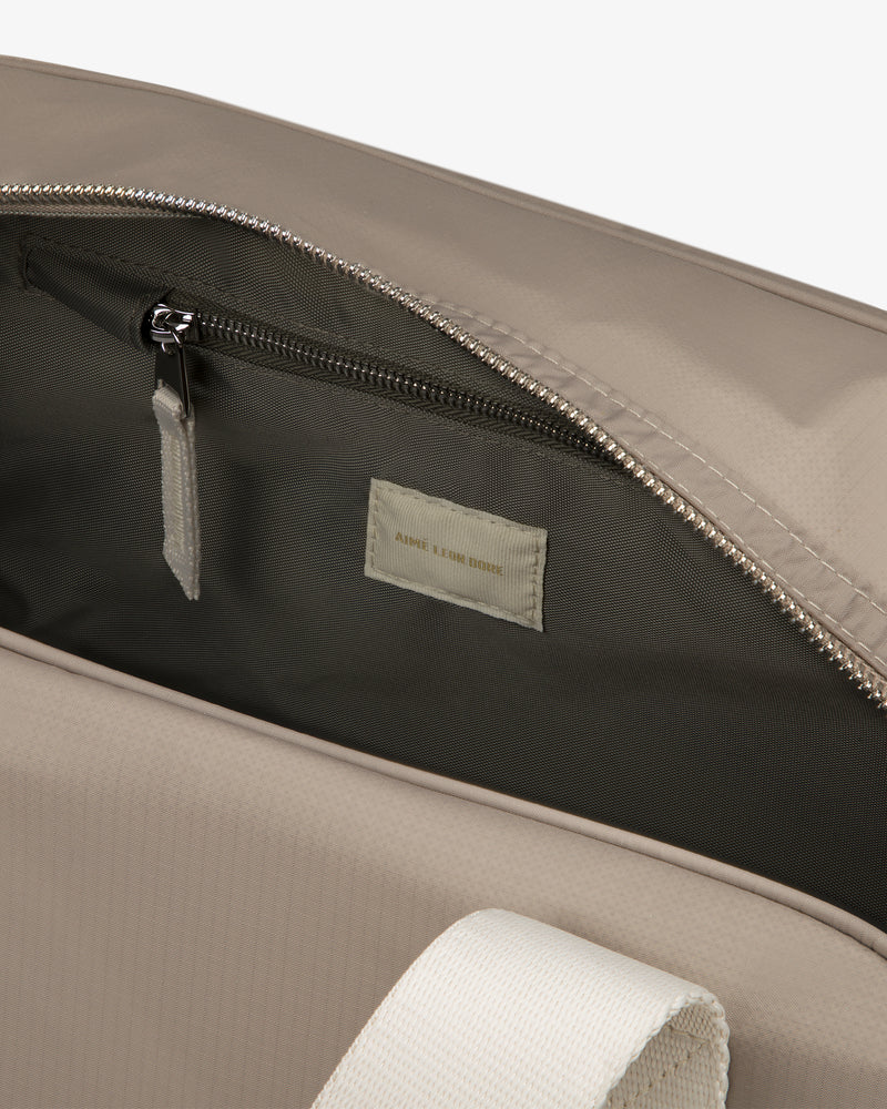 Close-up of the Nylon Duffle Bag in beige, featuring a white handle, open zipper, and inner pocket with fabric label.