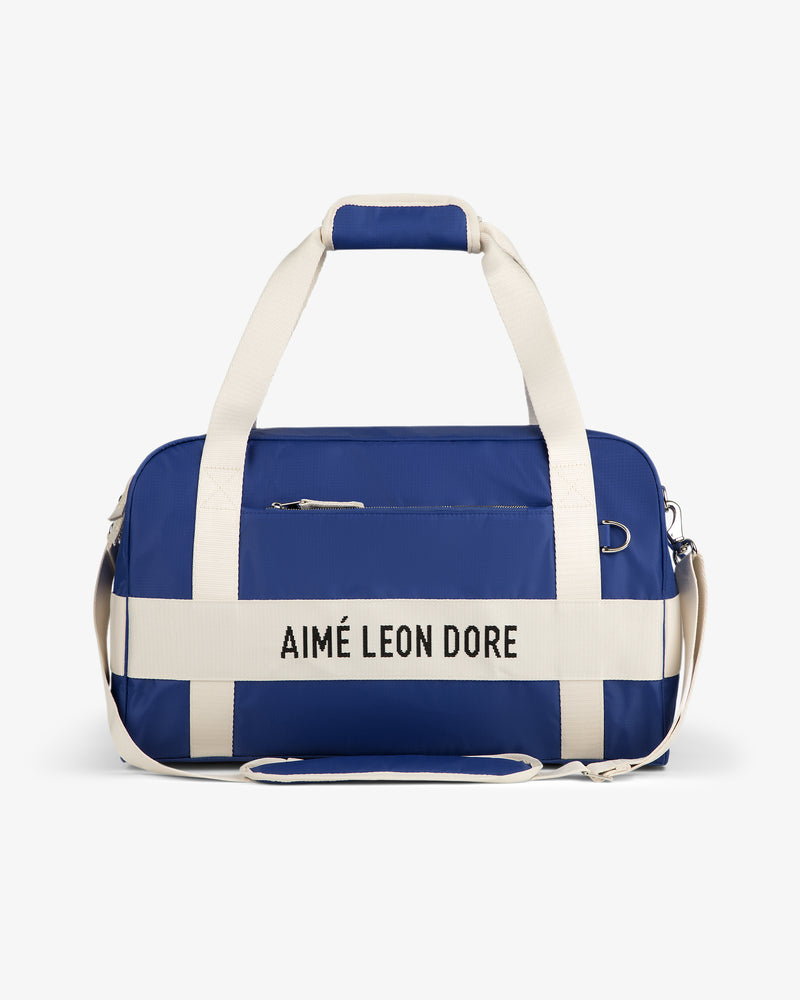Blue Nylon Duffle Bag with white straps and AIMÉ LEON DORE text on the front, shown on a white background.