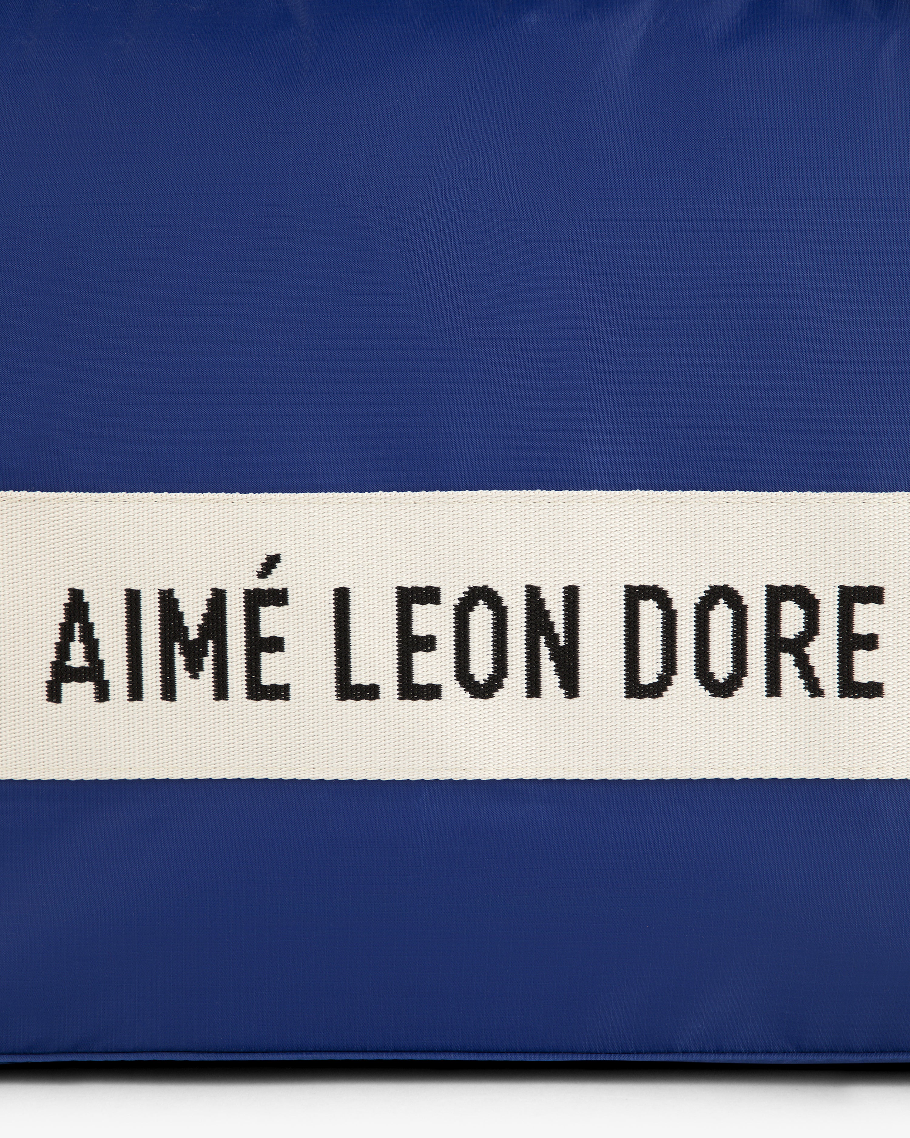 Blue nylon duffle bag with a white center stripe and black AIMÉ LEON DORE text.