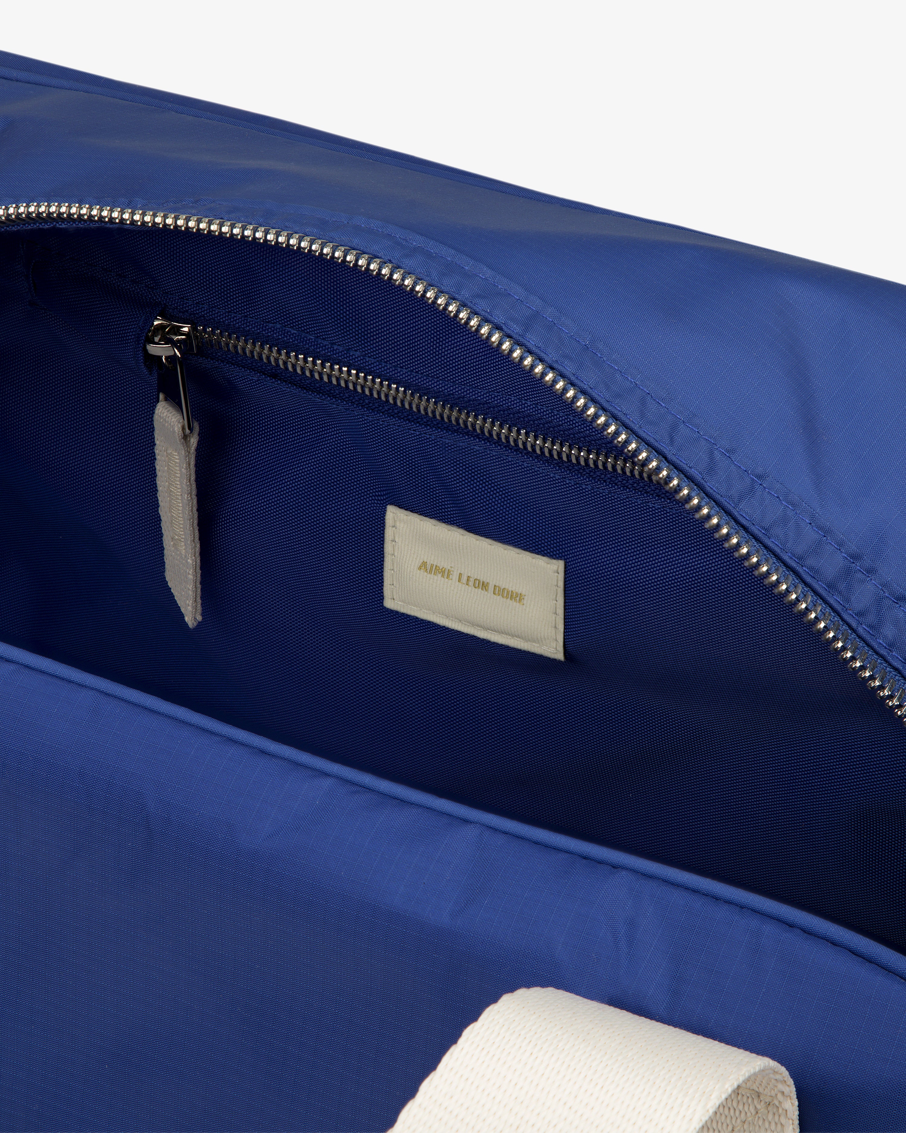 A close-up of a blue Nylon Duffle Bag’s interior with a zip pocket and a white AIMÉ LEON DORE label.