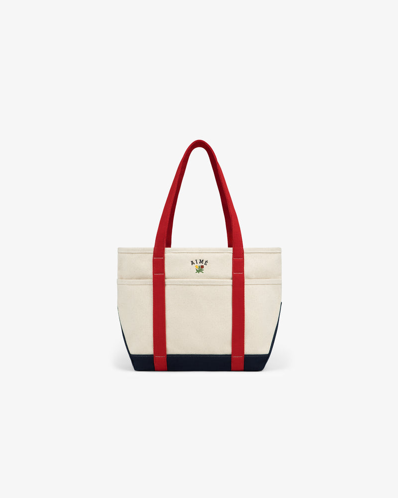 Small Crest Contrast Tote Bag in beige canvas with red handles, black base, and front embroidered logo.