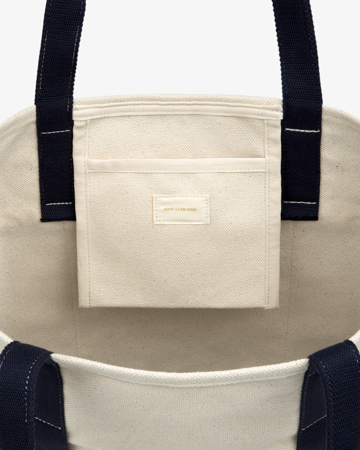 Large Crest Contrast Tote Bag: cream canvas, black straps, inner pocket, and a small gold label detail.