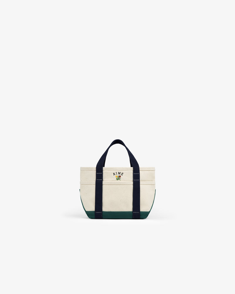 The Mini Crest Contrast Tote Bag is a small canvas bag with navy handles, green base, and front floral logo.