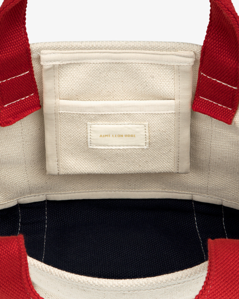 Mini Crest Contrast Tote Bag with red handles, inner pocket, and AIME LEON DORE stitched in gold on the pocket.