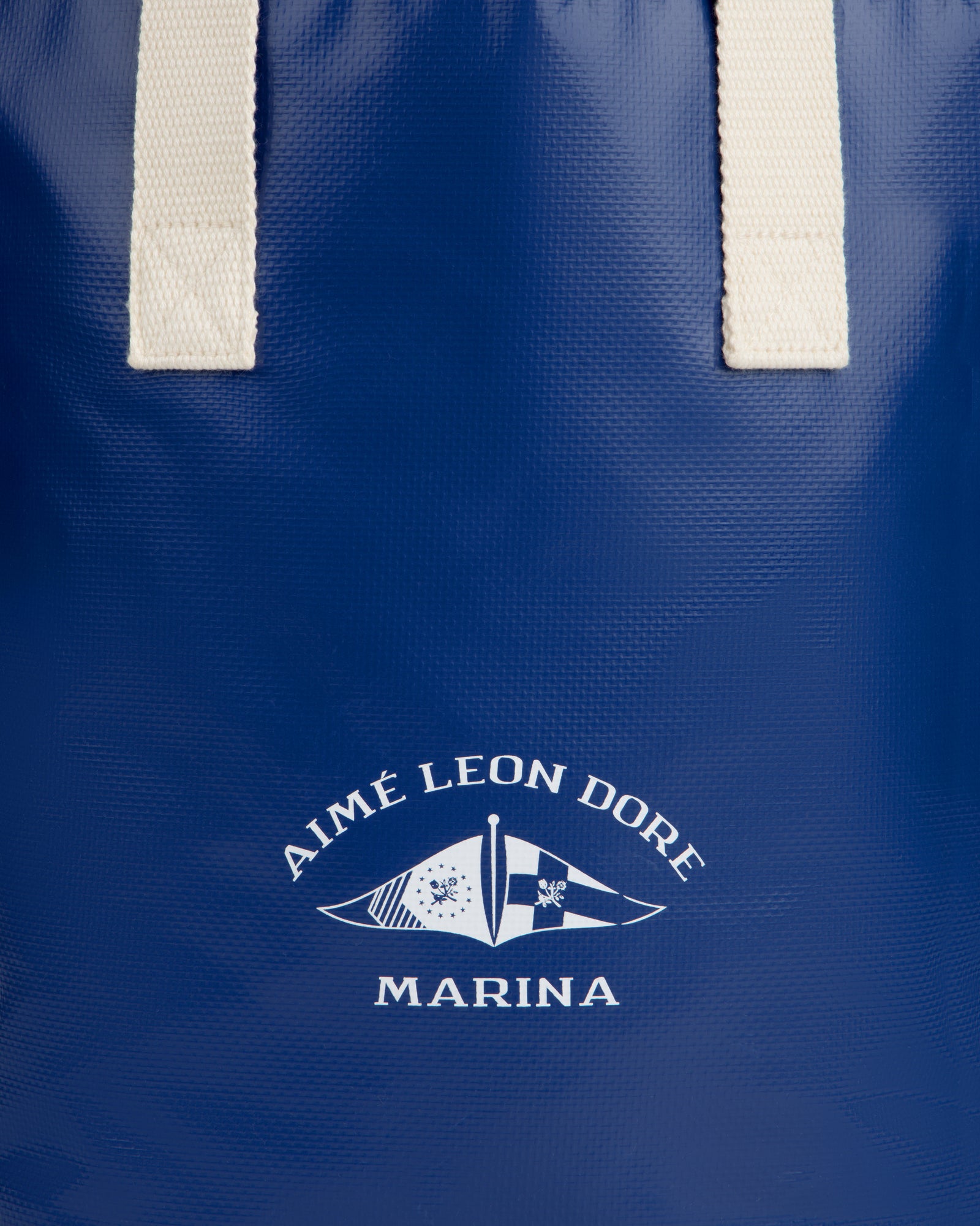 Close-up of the Marina Bottle Tote in blue with white handles and Aimé Leon Dore Marina nautical flag logo.