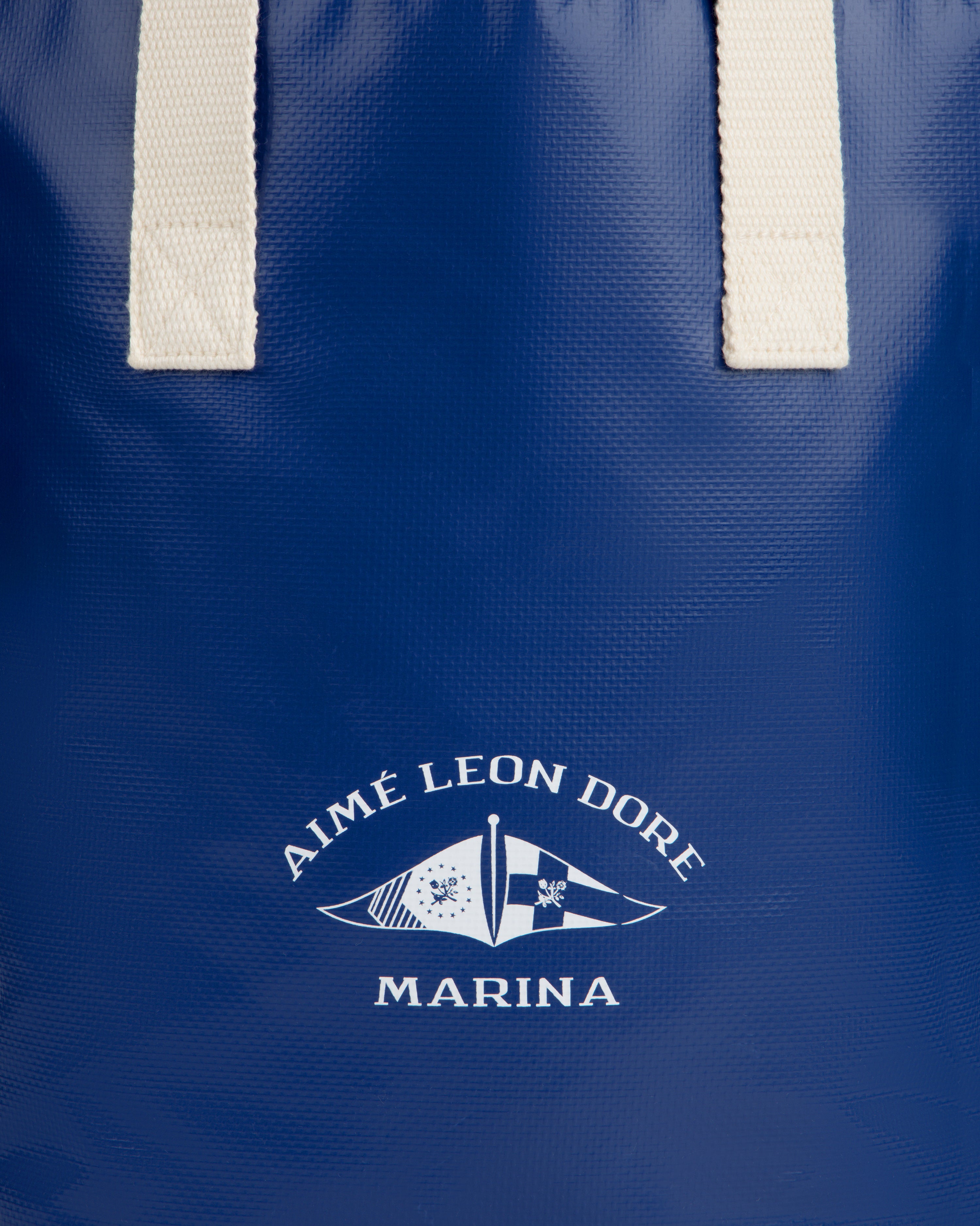 Close-up of the Marina Bottle Tote in blue with white handles and Aimé Leon Dore Marina nautical flag logo.
