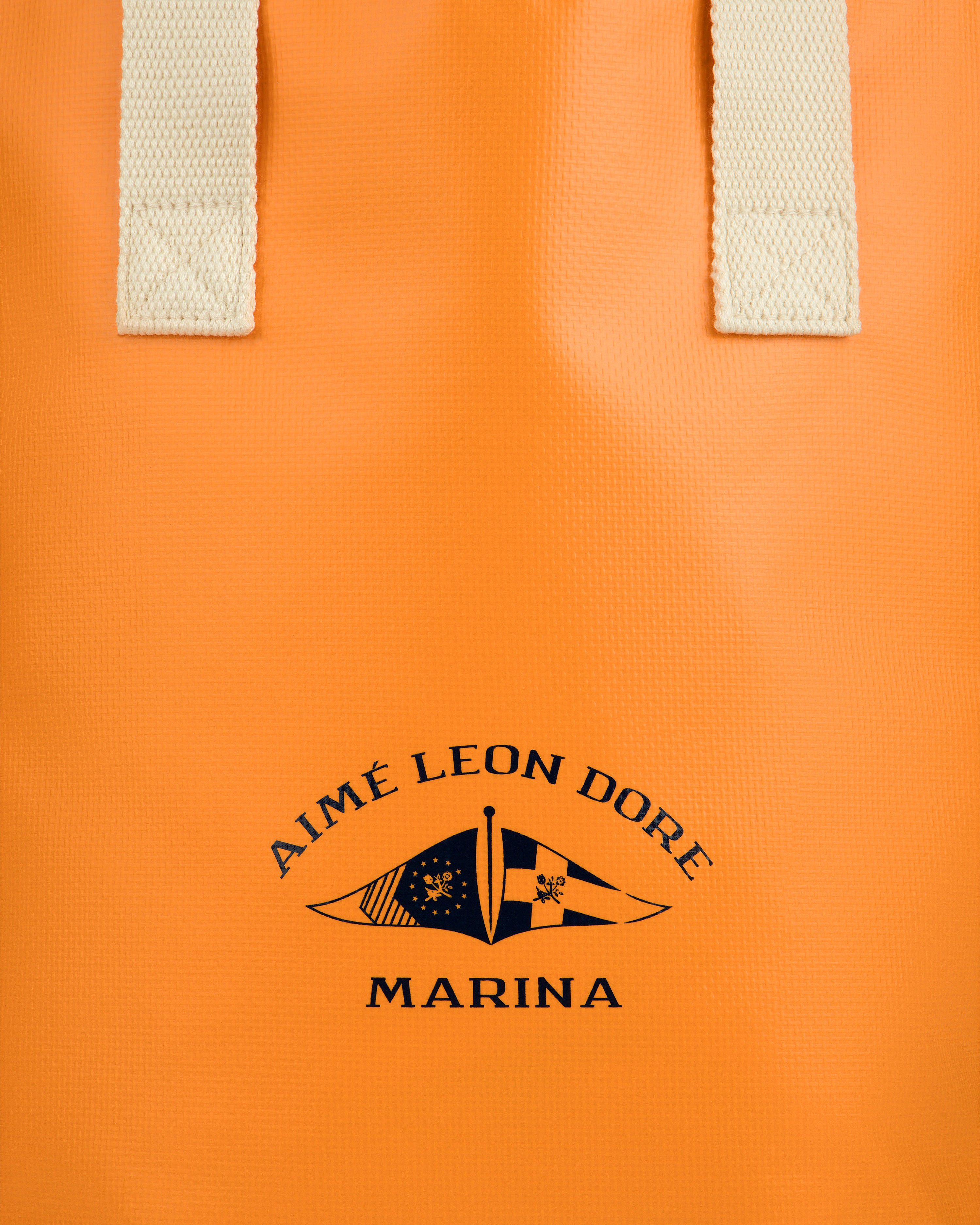Close-up of the Marina Bottle Tote—an orange bag with cream handles and a navy AIMÉ LEON DORE MARINA logo and flags.
