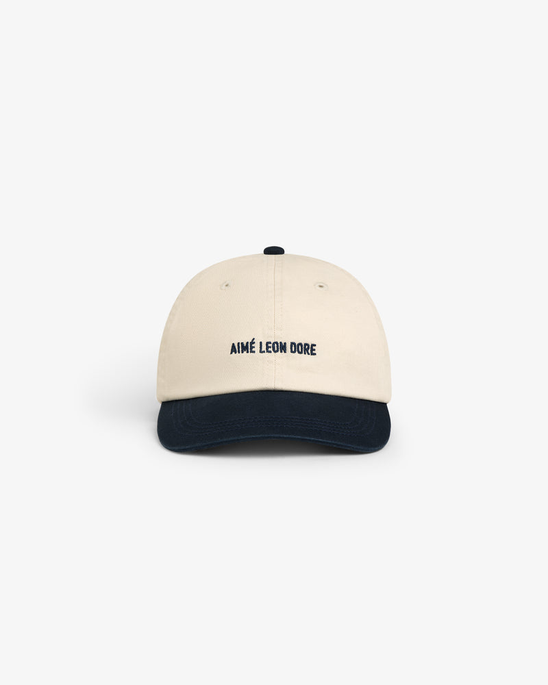 Washed Chino Hat in beige with a navy blue brim and AIMÉ LEON DORE embroidered on the front.