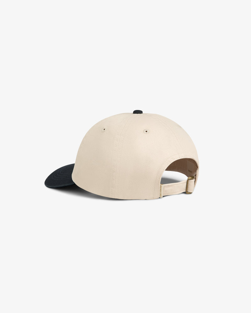 The Washed Chino Hat is a beige baseball cap with a black brim and adjustable strap, shown from the back.