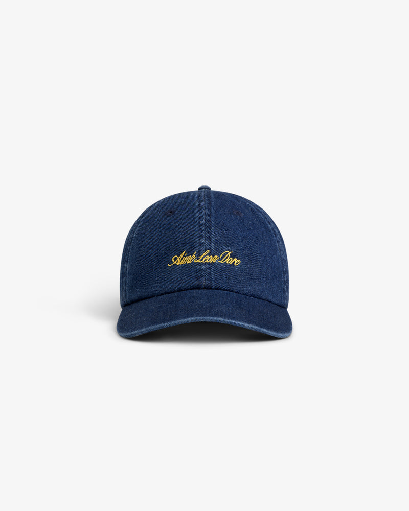 The Denim Script Hat is a dark blue denim baseball cap with yellow embroidered cursive text on the front.