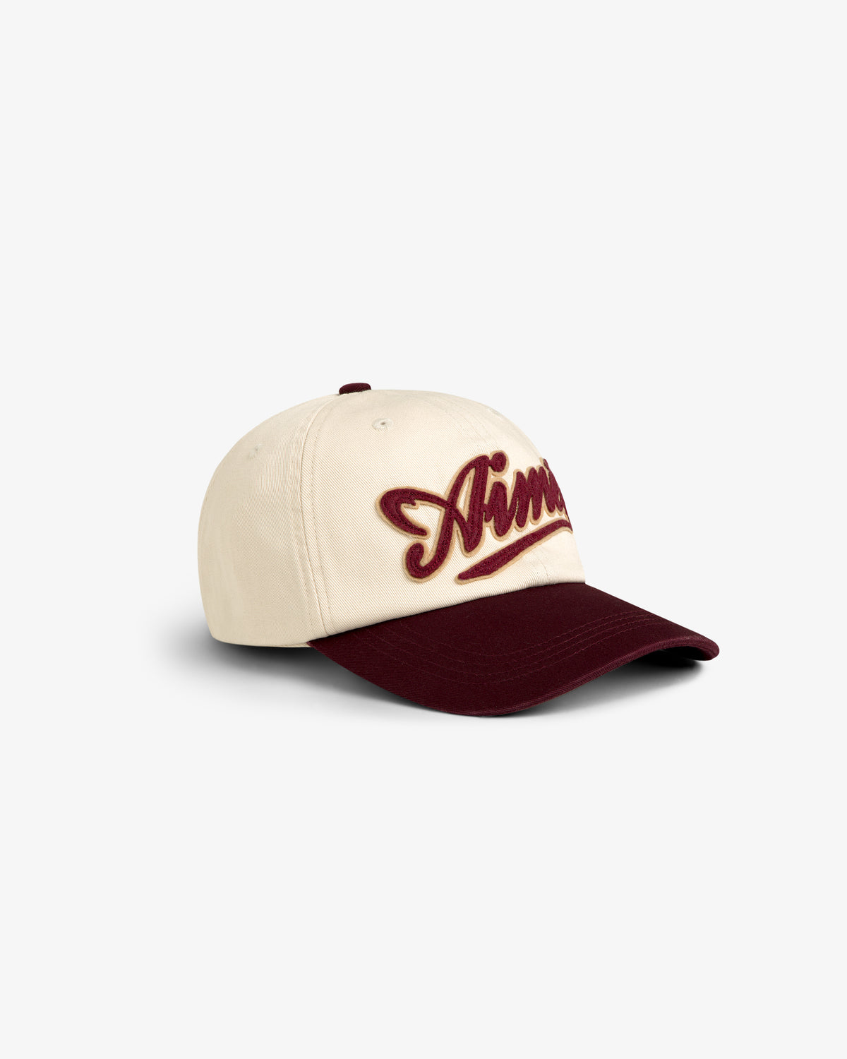 The Cycling Logo Hat is a cream cap with a burgundy visor and bold burgundy script embroidery on the front.