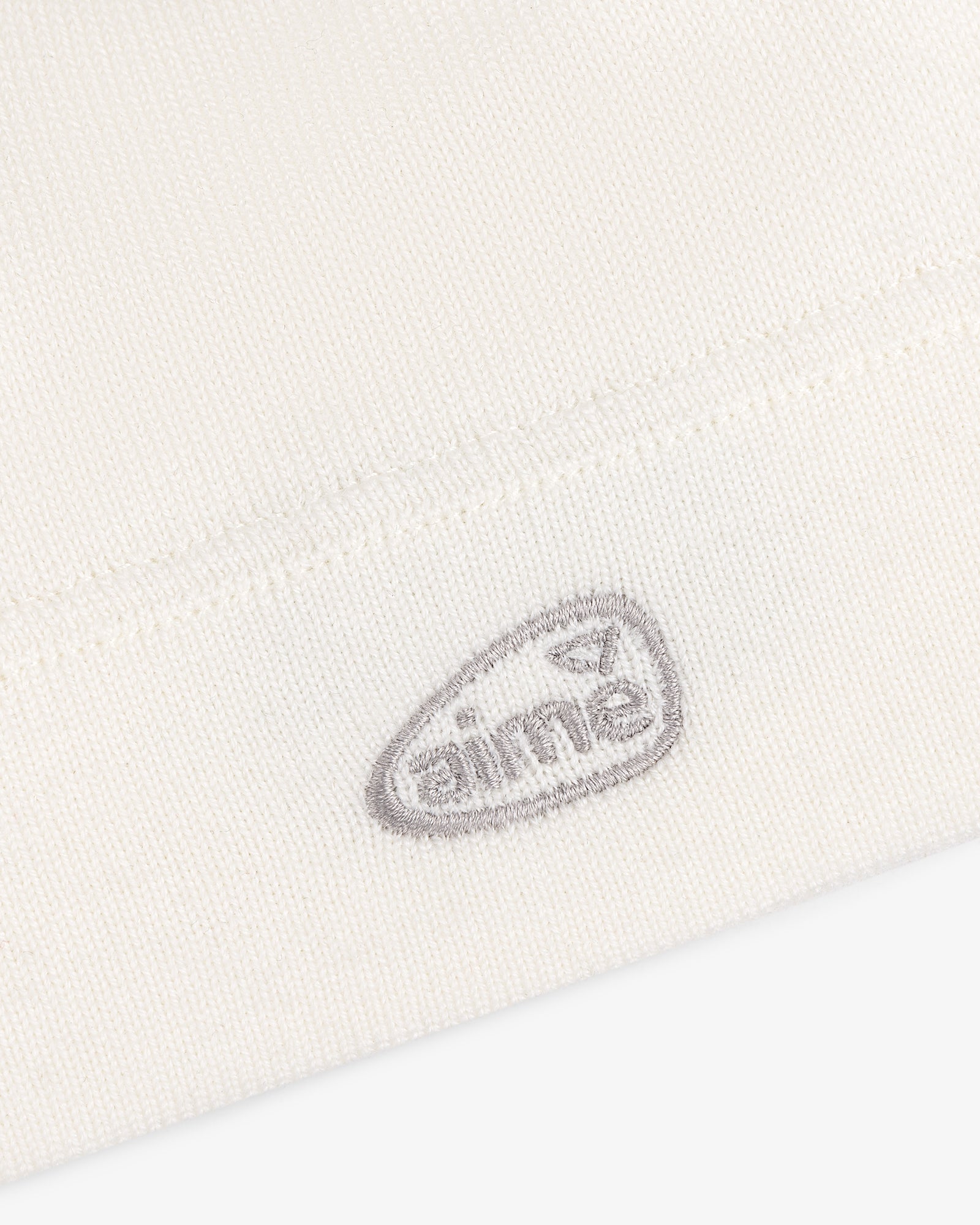 Close-up of a white ALD Golf Skull Cap with a small, gray embroidered oval logo that reads AIME.