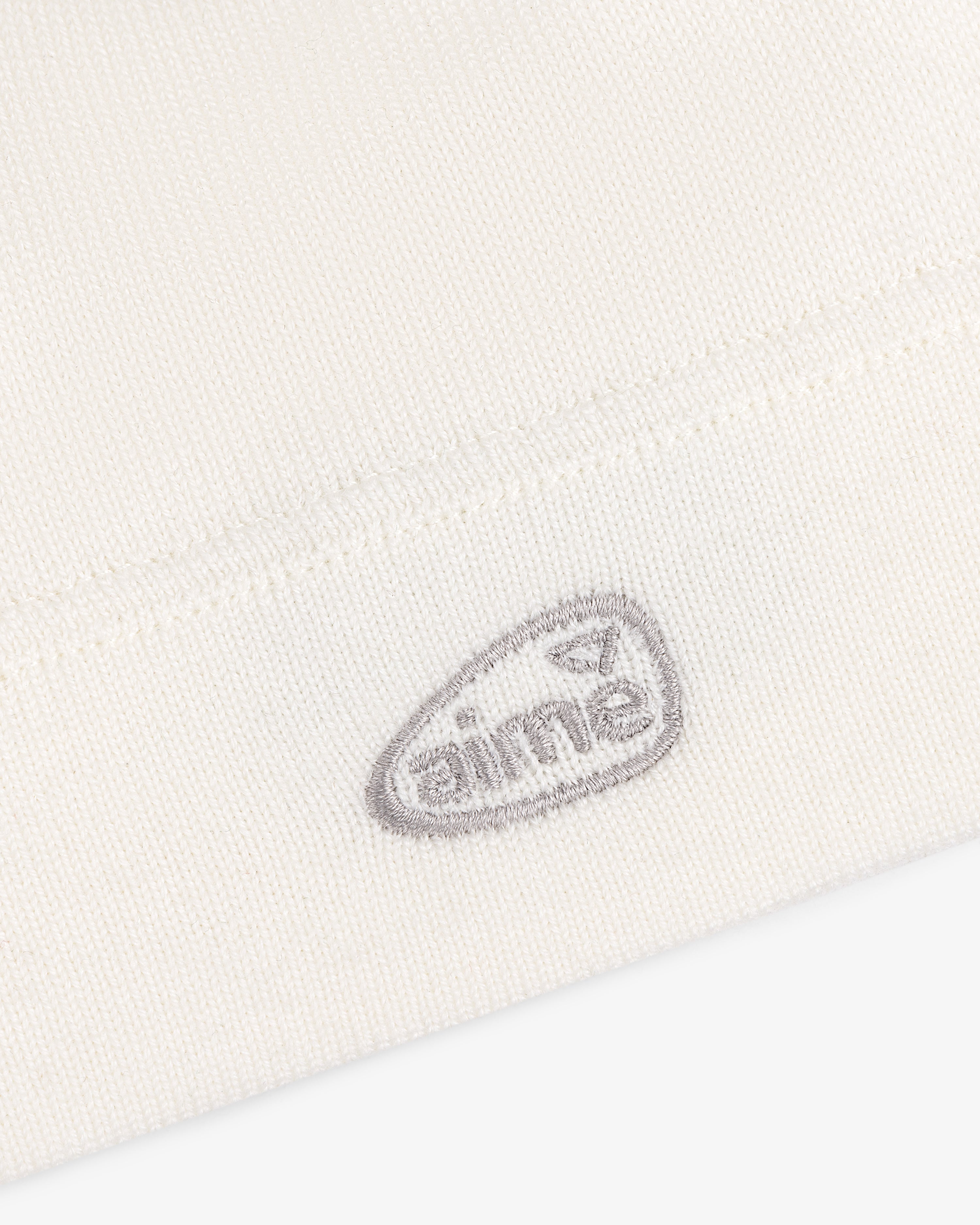 Close-up of a white ALD Golf Skull Cap with a small, gray embroidered oval logo that reads AIME.