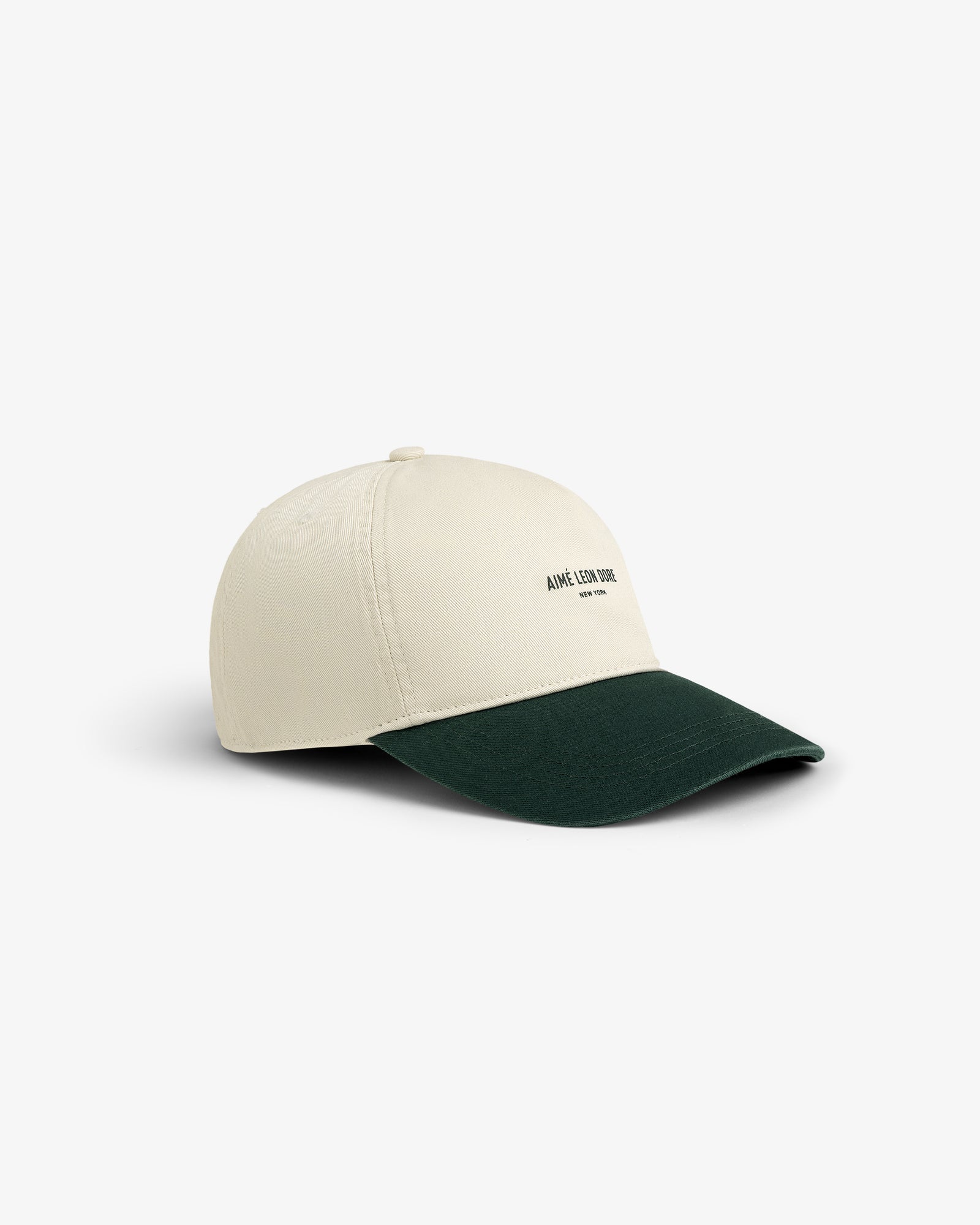 Micro Logo Hat: beige cap with dark green brim, small black text logo on front, shown on white background.