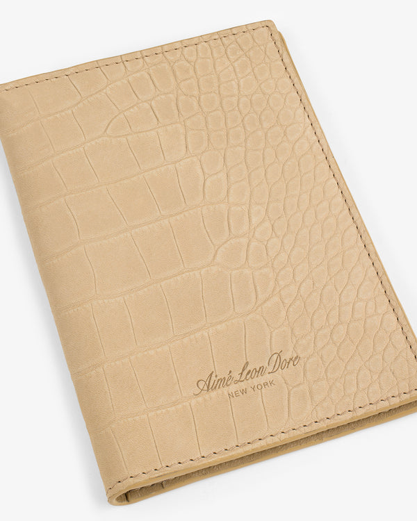 Beige croc-embossed nubuck passport holder with Aimé Leon Dore New York embossed on the front.