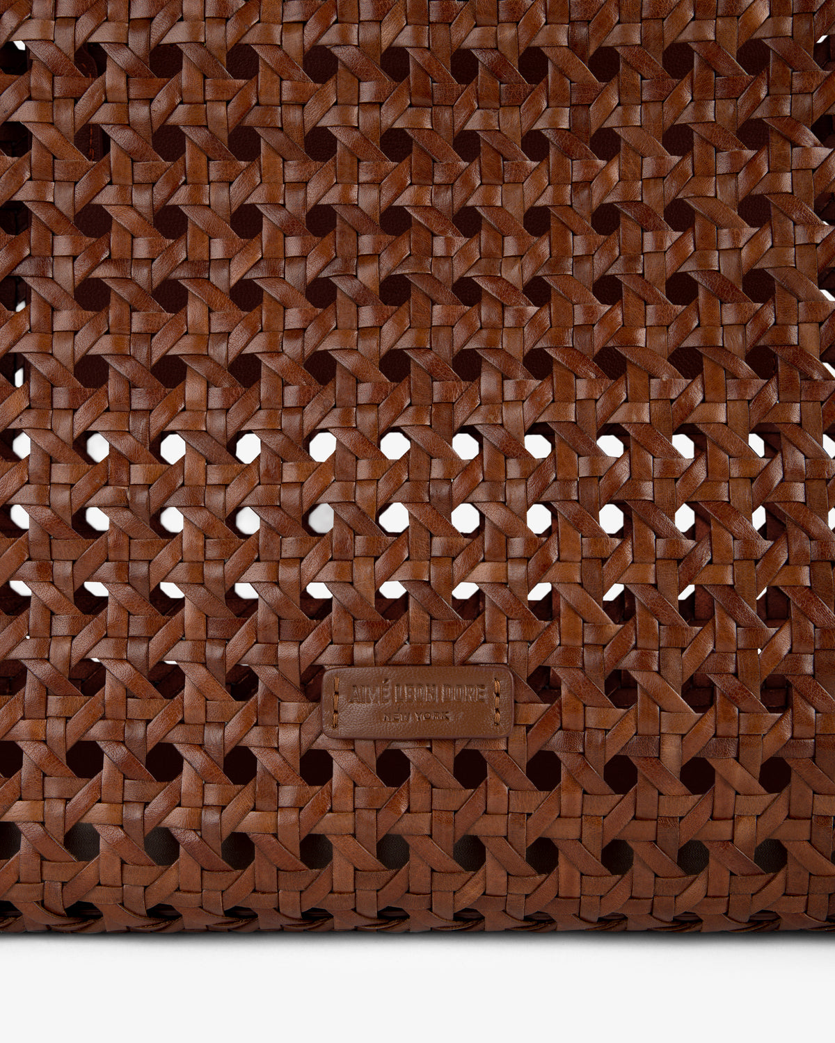 Close-up of the Woven Leather Tote Bag’s brown woven leather pattern with a small leather tag near the bottom center.