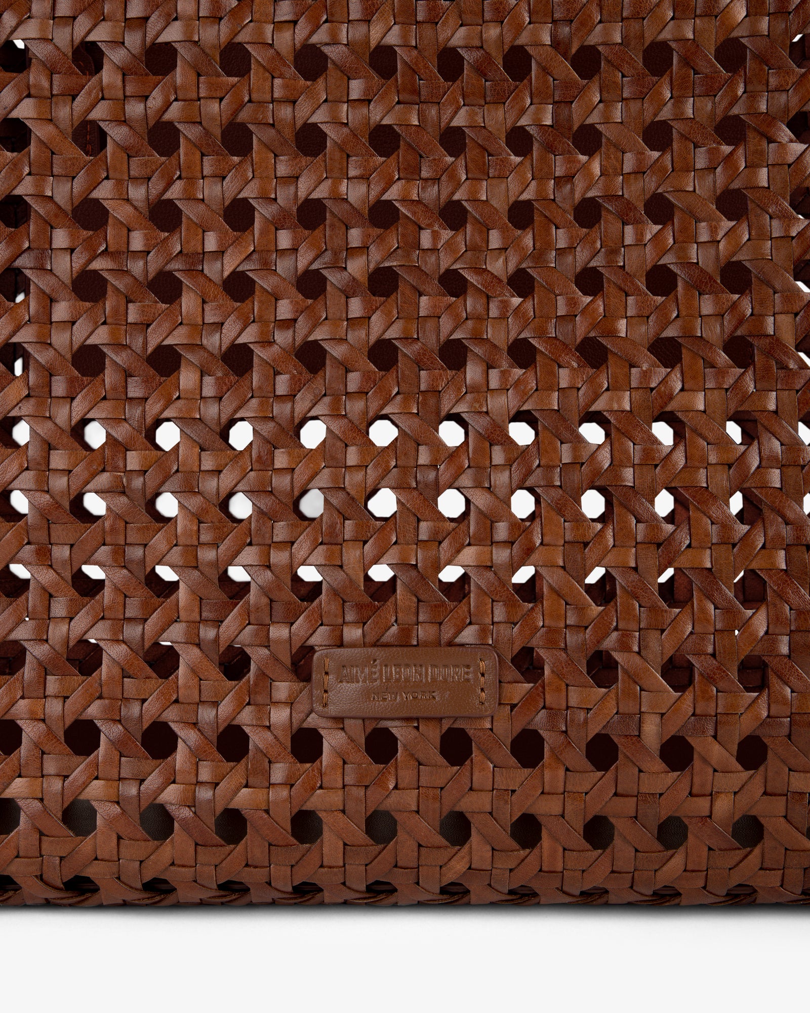 Close-up of the Woven Leather Tote Bag’s brown woven leather pattern with a small leather tag near the bottom center.