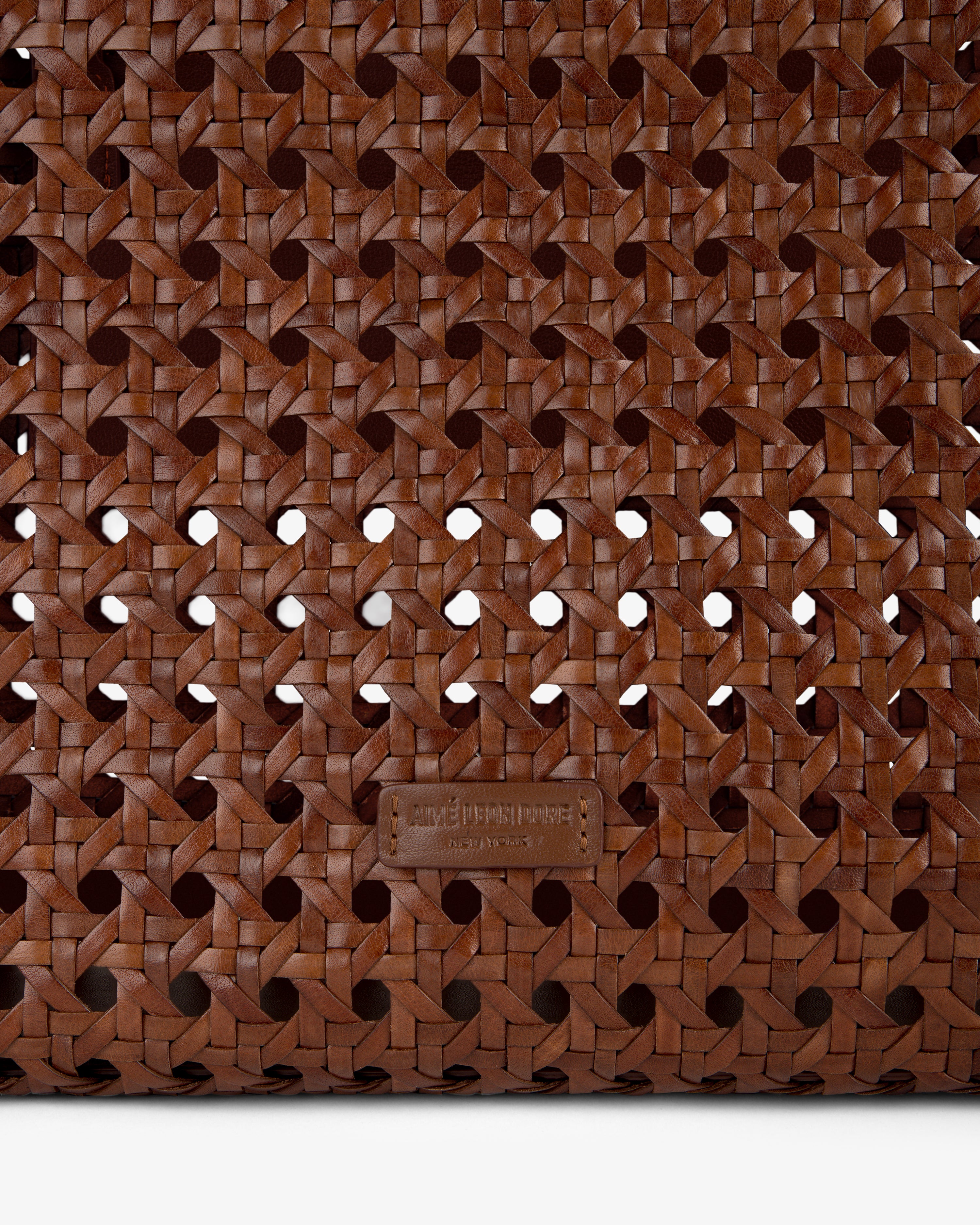 Close-up of the Woven Leather Tote Bag’s brown woven leather pattern with a small leather tag near the bottom center.