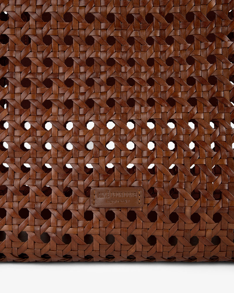 Close-up of the Woven Leather Tote Bag’s brown woven leather pattern with a small leather tag near the bottom center.