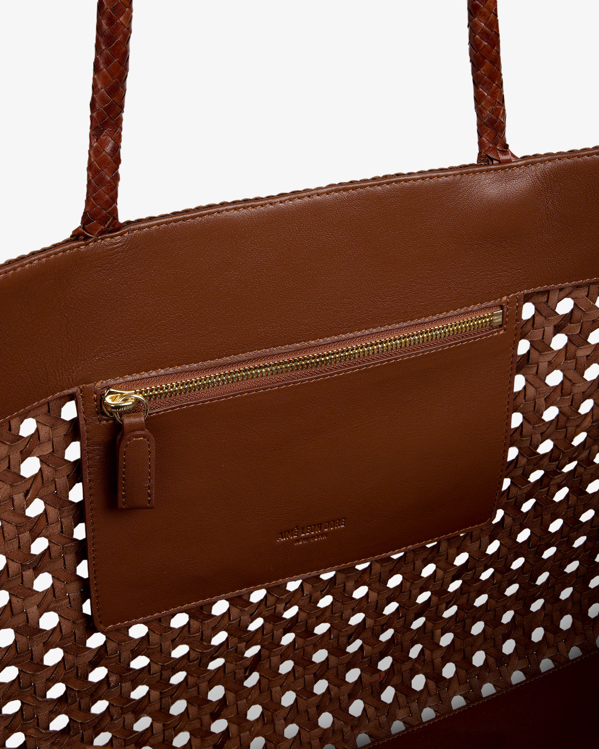 Close-up of the Woven Leather Tote Bag in brown, featuring an interior zip pocket and gold zipper accents.