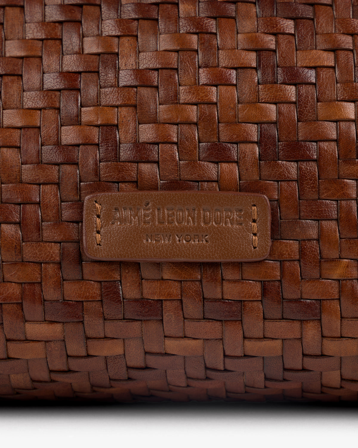 Close-up of a brown Woven Leather Shoulder Bag with an AIMÉ LEON DORE NEW YORK label stitched on the front.