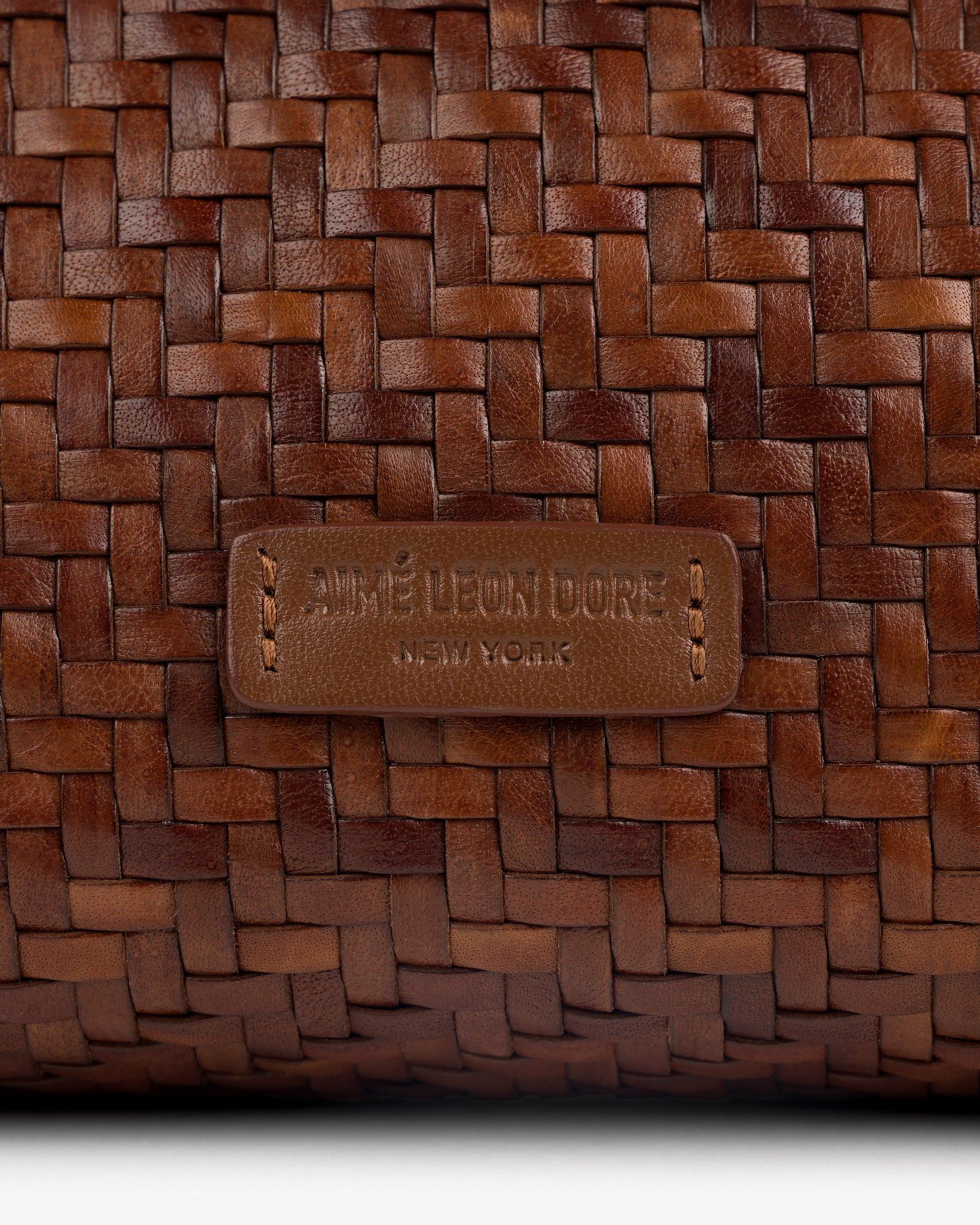 Close-up of a brown Woven Leather Shoulder Bag with an AIMÉ LEON DORE NEW YORK label stitched on the front.
